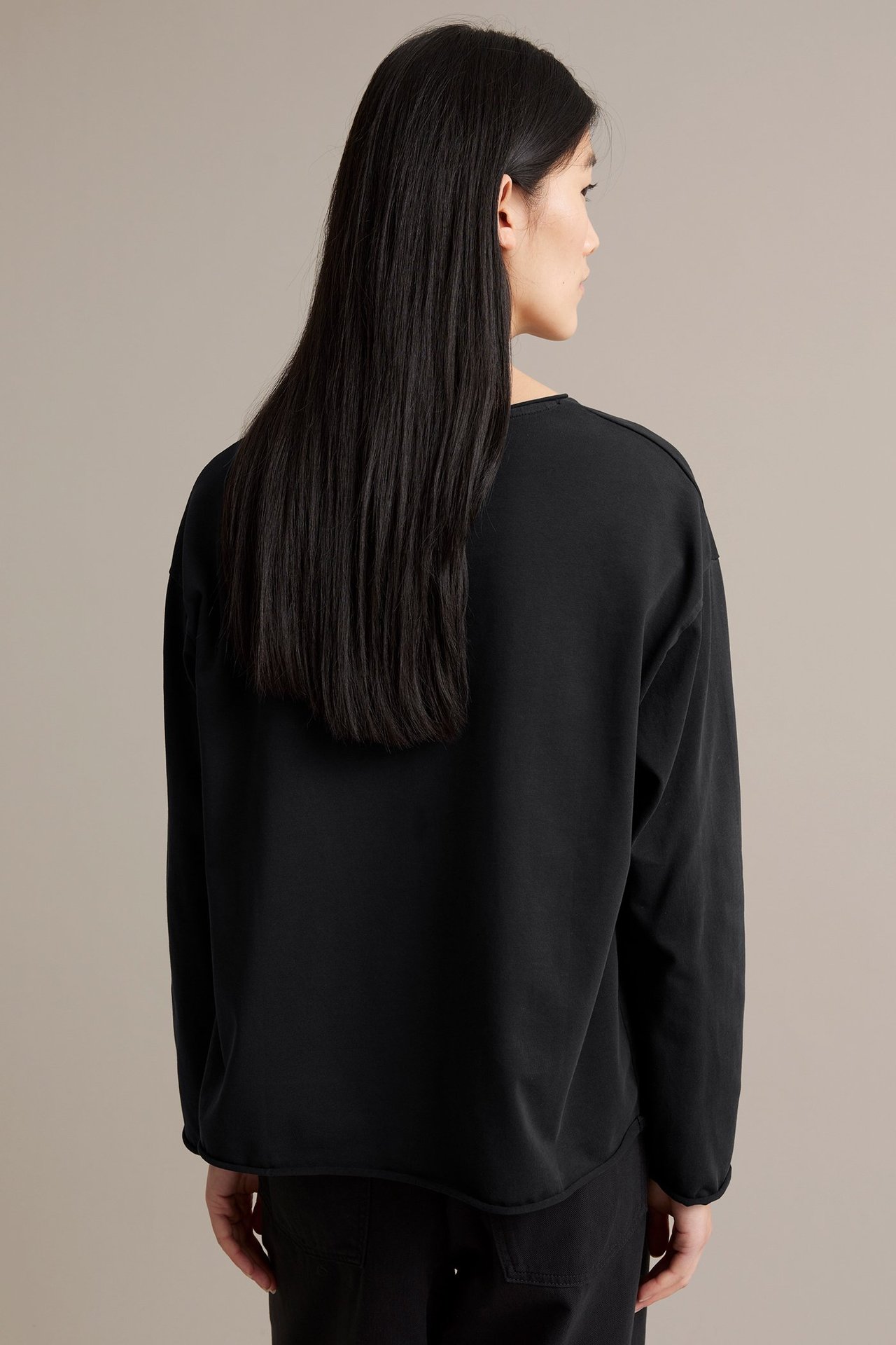 Kvinna i svart långärmad tröja i kraftig trikå med råa kanter och tvättad look, baksida.