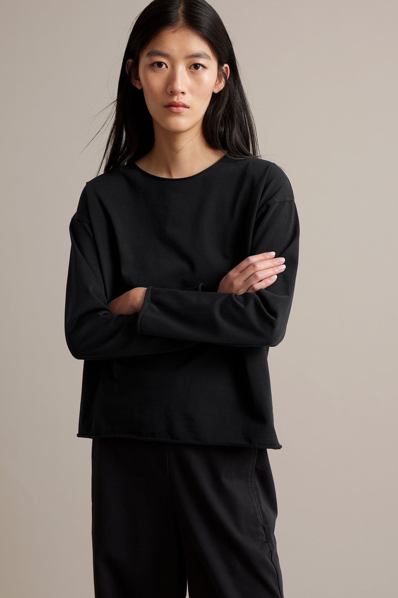 Musta pitkähihainen paita paksusta jerseystä, raaka reunat, pesun näköinen, naisella edessä.