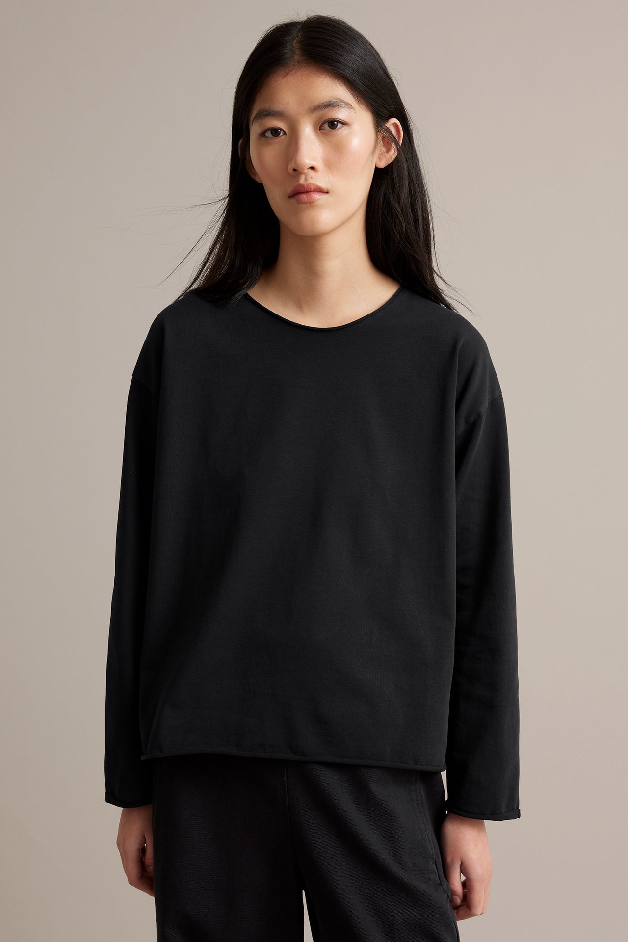 Svart långärmad top i kraftig trikå med råa kanter, utsliten look, kvinna frontvy.