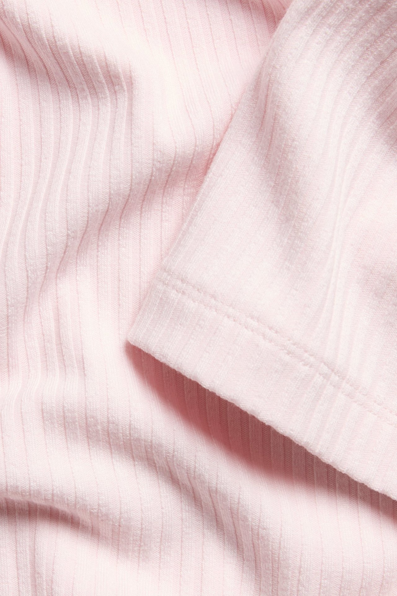 Zbliżenie na jasnoróżowy, prążkowany materiał topu, pokazujące teksturę dzianiny i obszyty brzeg.