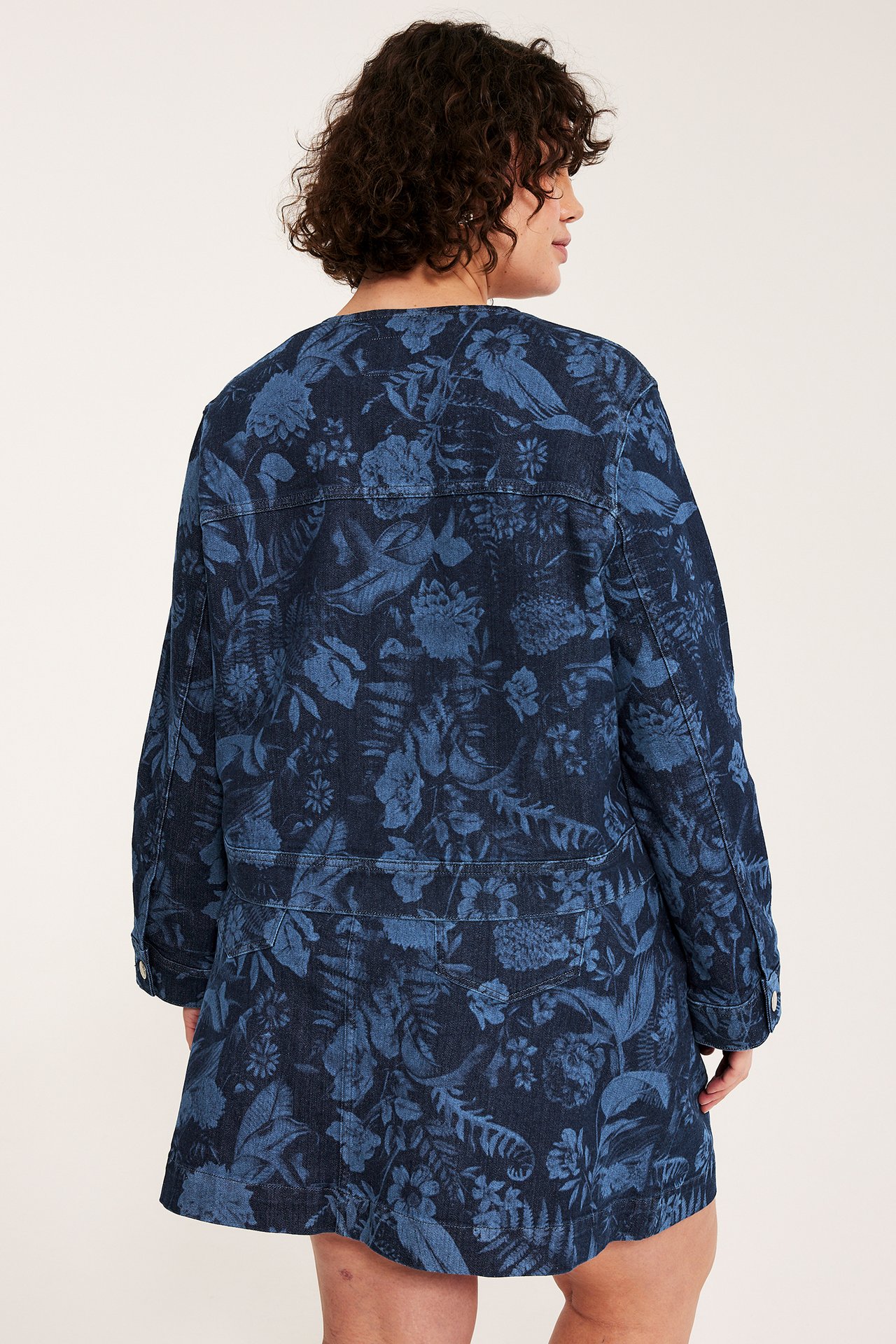 Widok z tyłu kobiety w granatowej kurtce jeansowej z jasnoniebieskim kwiatowym wzorem.