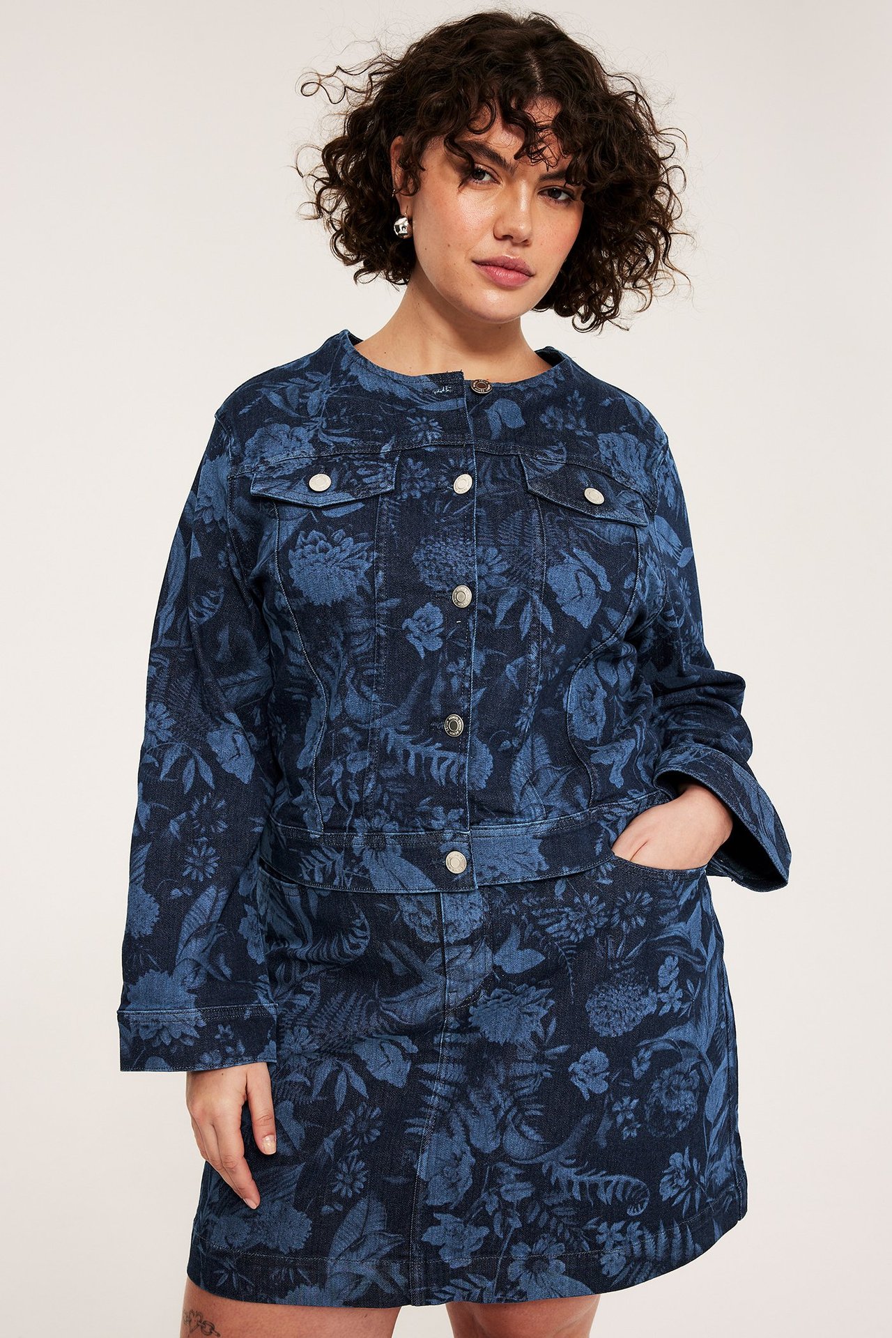 Framsida, kvinna bär en mörkblå blommig jeansjacka med matchande kjol.