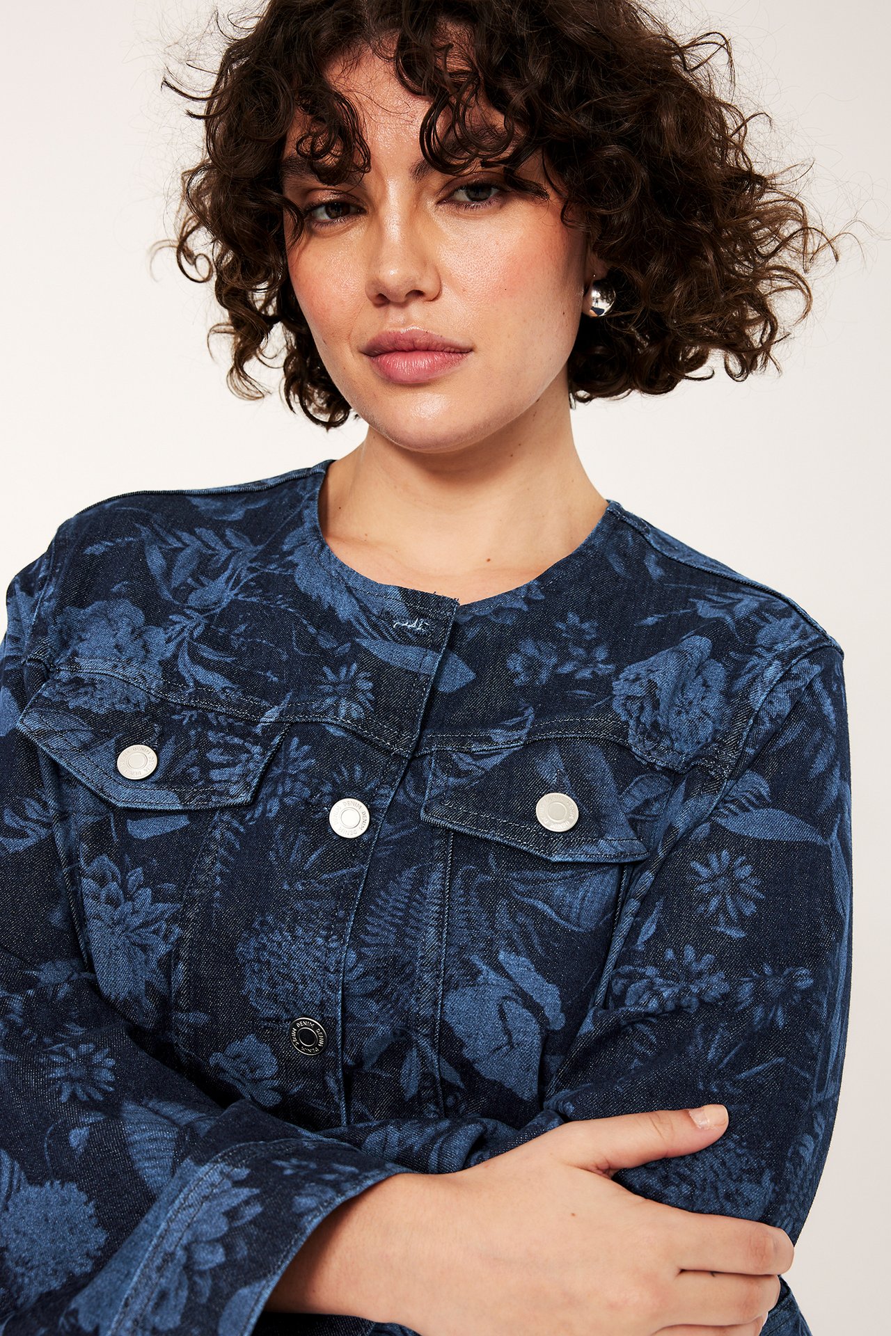 Zbliżenie z przodu kobiety w granatowej jeansowej kurtce w kwiaty, ze srebrnymi guzikami i kolczykami.