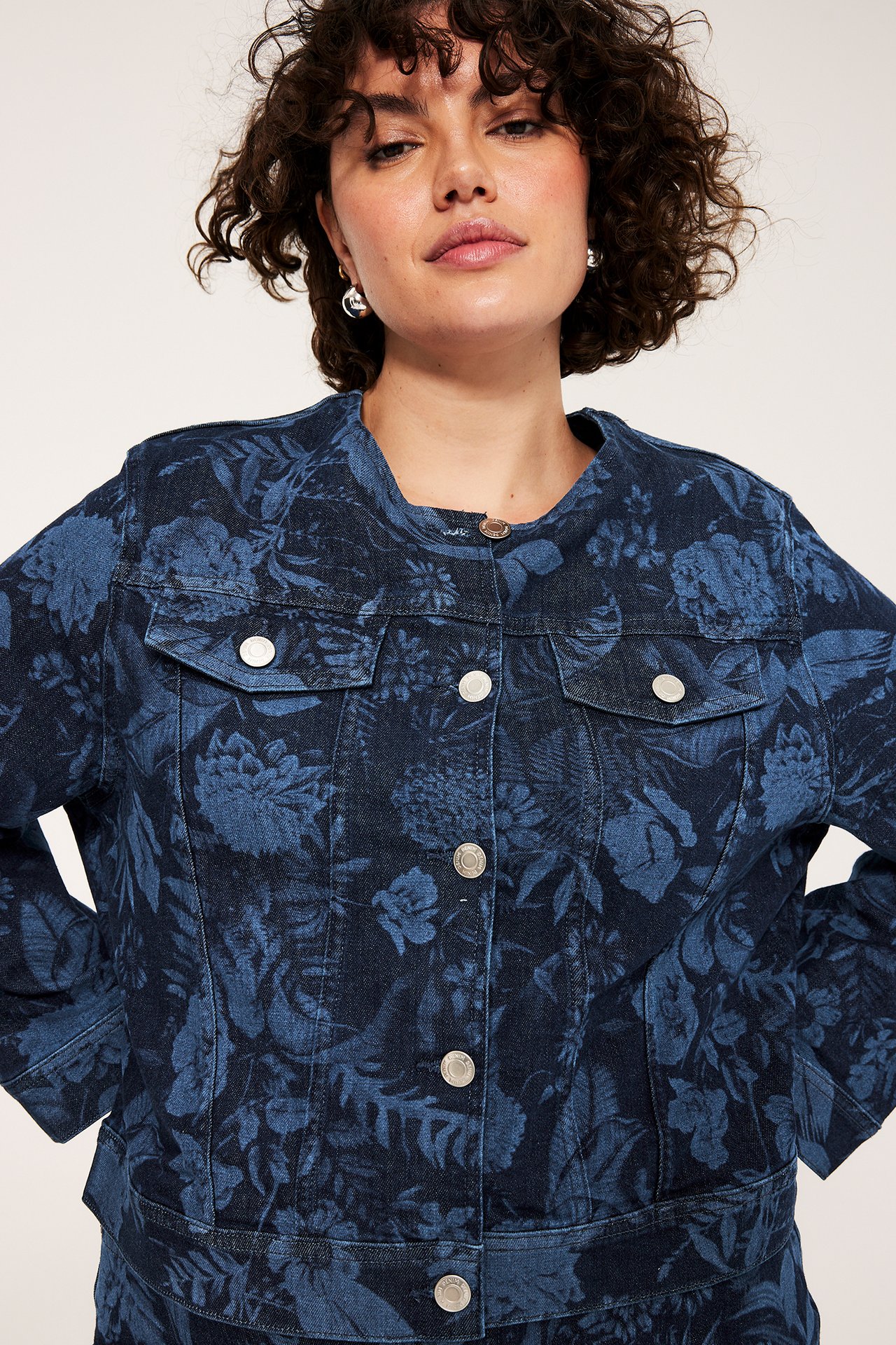 Widok z przodu: kobieta w ciemnoniebieskiej kurtce jeansowej w kwiaty ze srebrnymi guzikami i kolczykami.