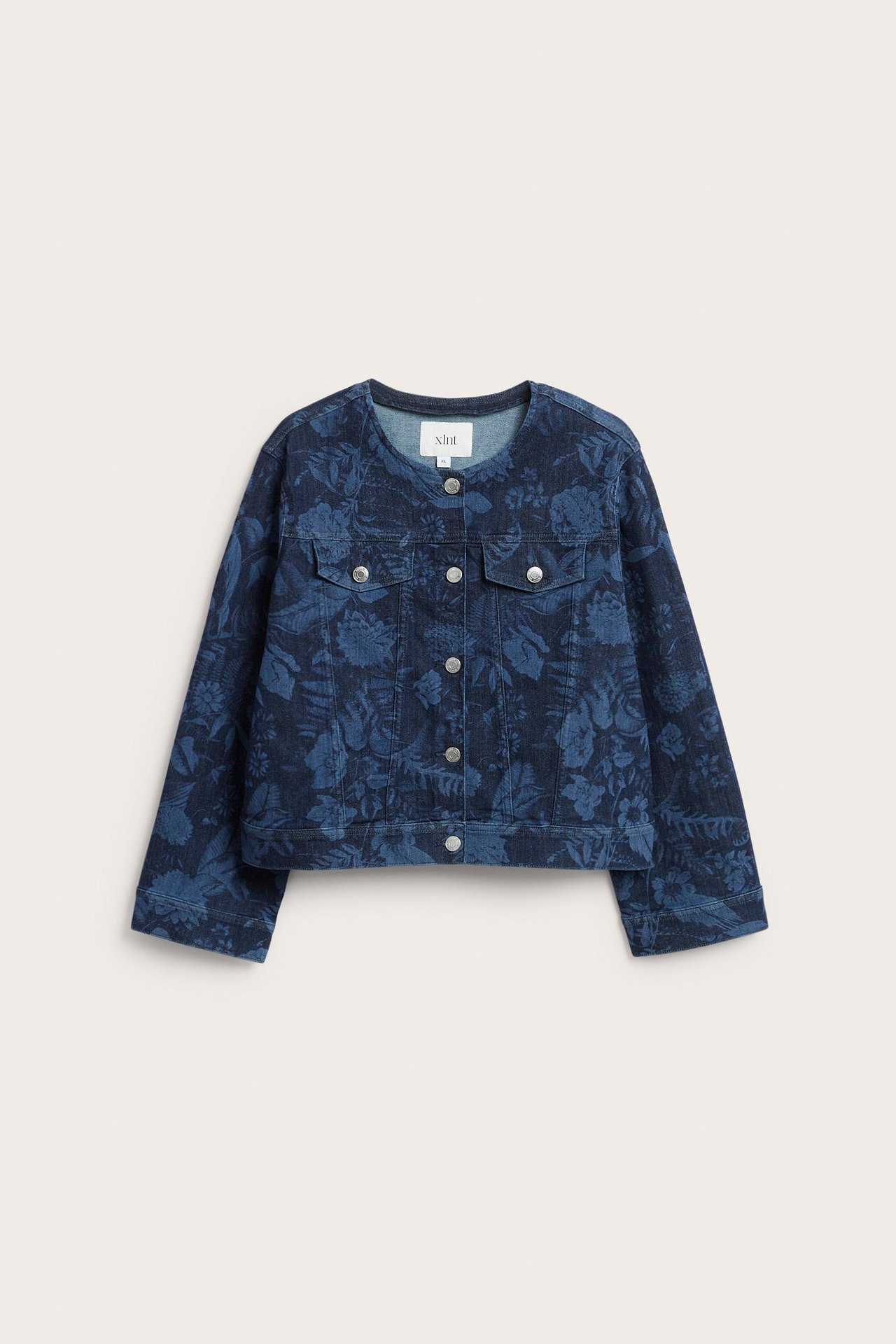 Framsida av en mörkblå blommig jeansjacka med kraglös design och silverfärgade knappar fram.