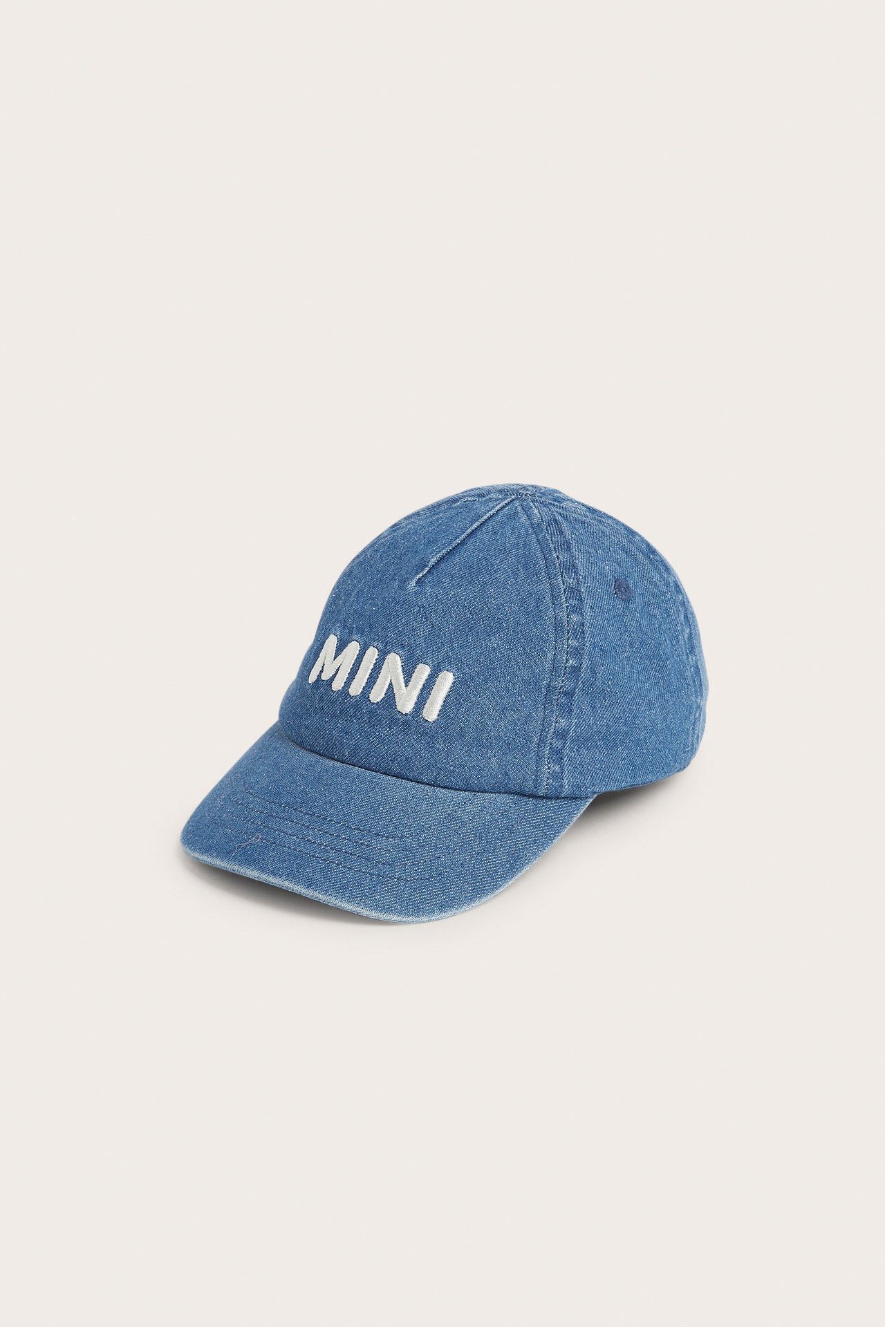3/4 frontvisning av en blå denimcaps med hvit "MINI"-broderi foran og elastisk rygg.
