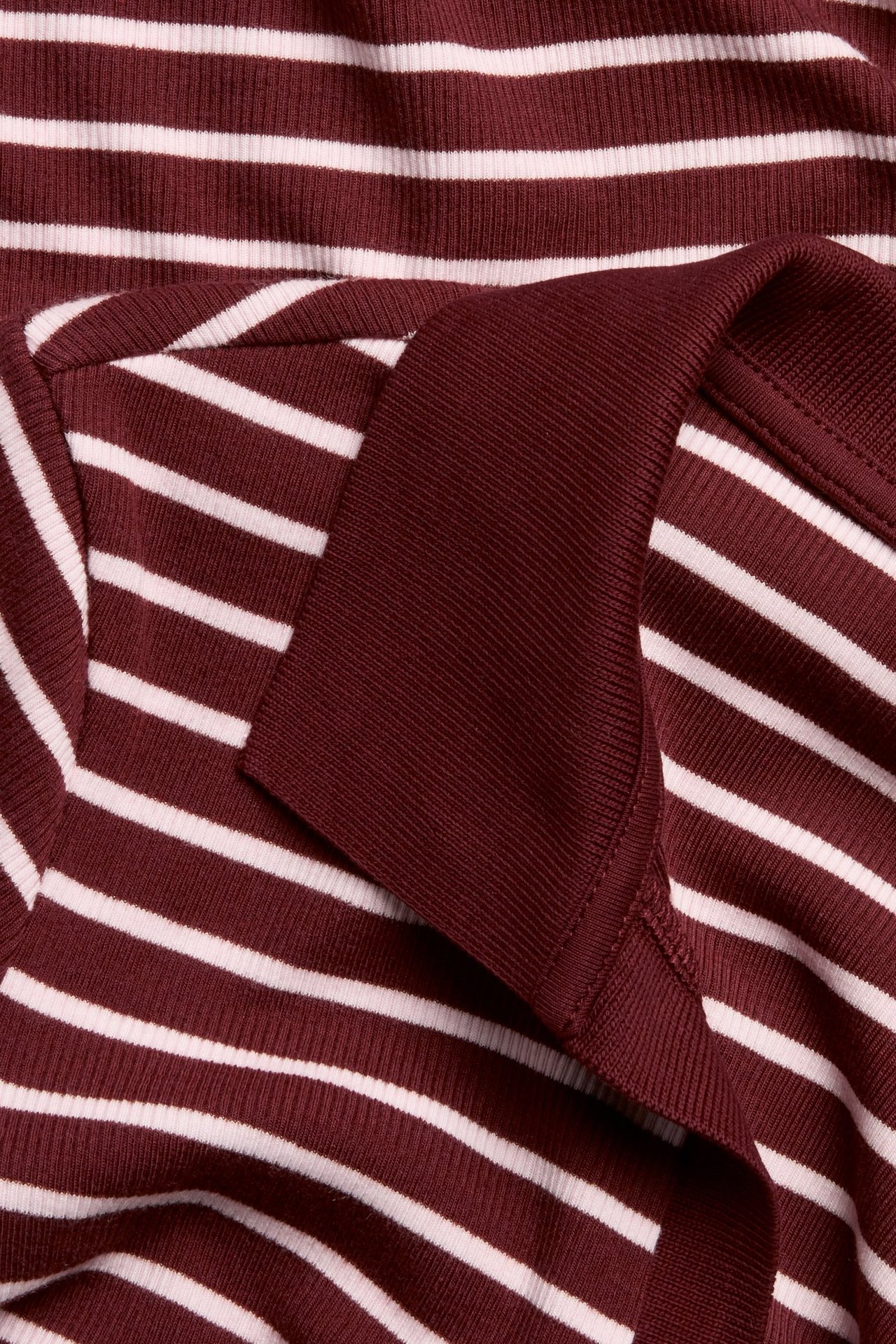 Zbliżenie na czerwono-biały prążkowany top z krótkim rękawem, z jednolitym czerwonym kołnierzykiem polo i prążkowaną fakturą.