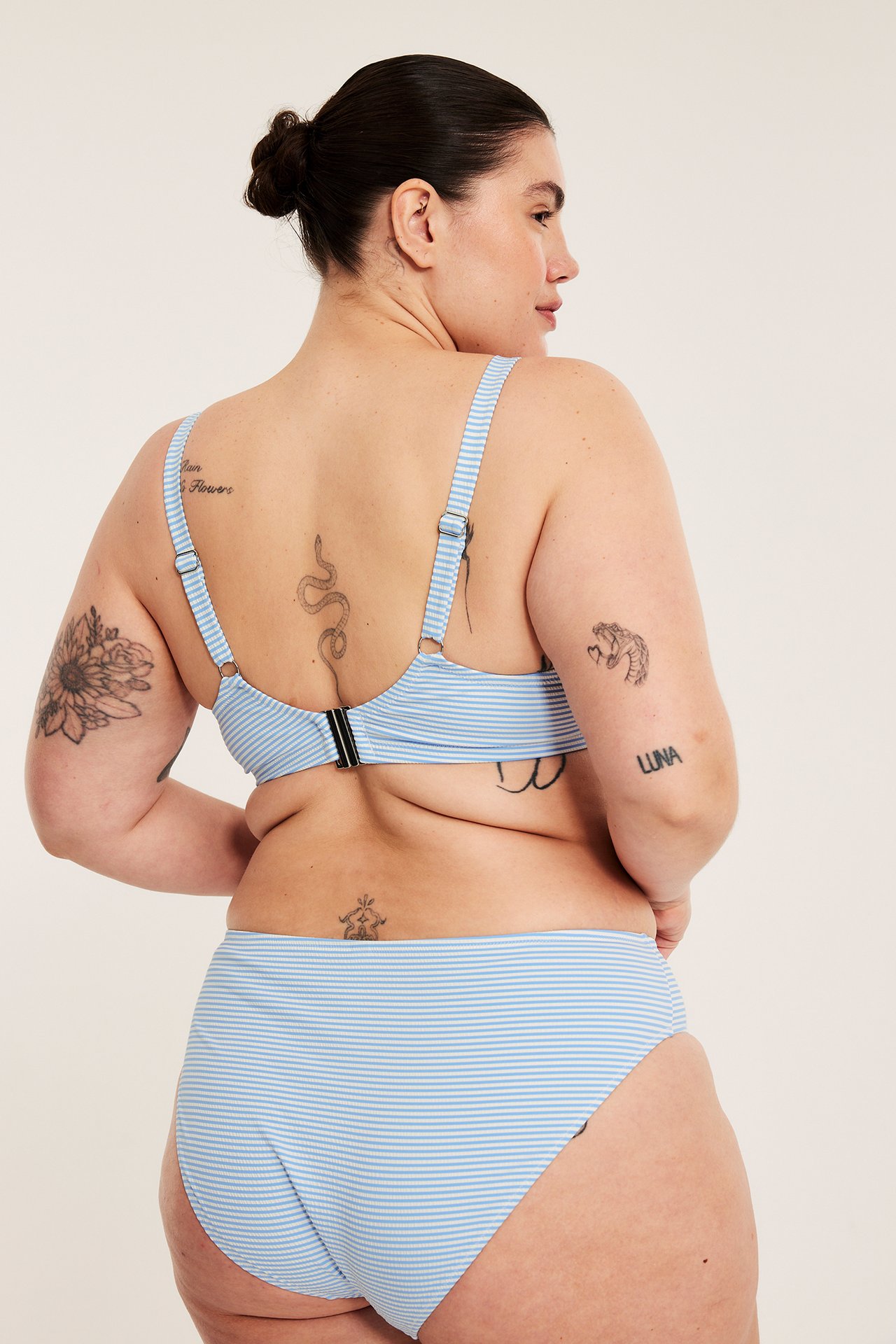 Selkäkuva: nainen vaaleansinisessä raidallisessa bikiniliivissä hakasella ja yhteensopivissa korkeavyötäröisissä bikininhousuissa.