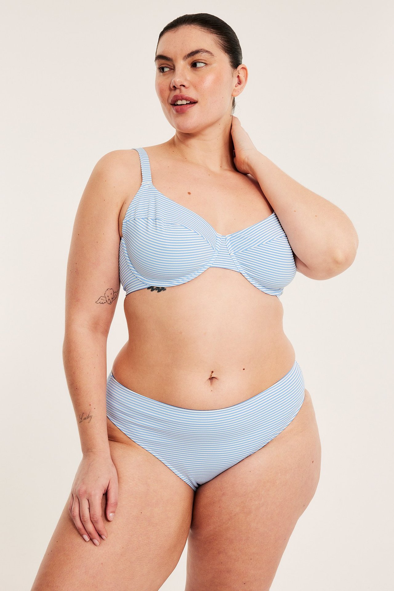 Frontbilde av en kvinne i en lys blå stripete bikinitopp og matchende høy midje bikinitruse.