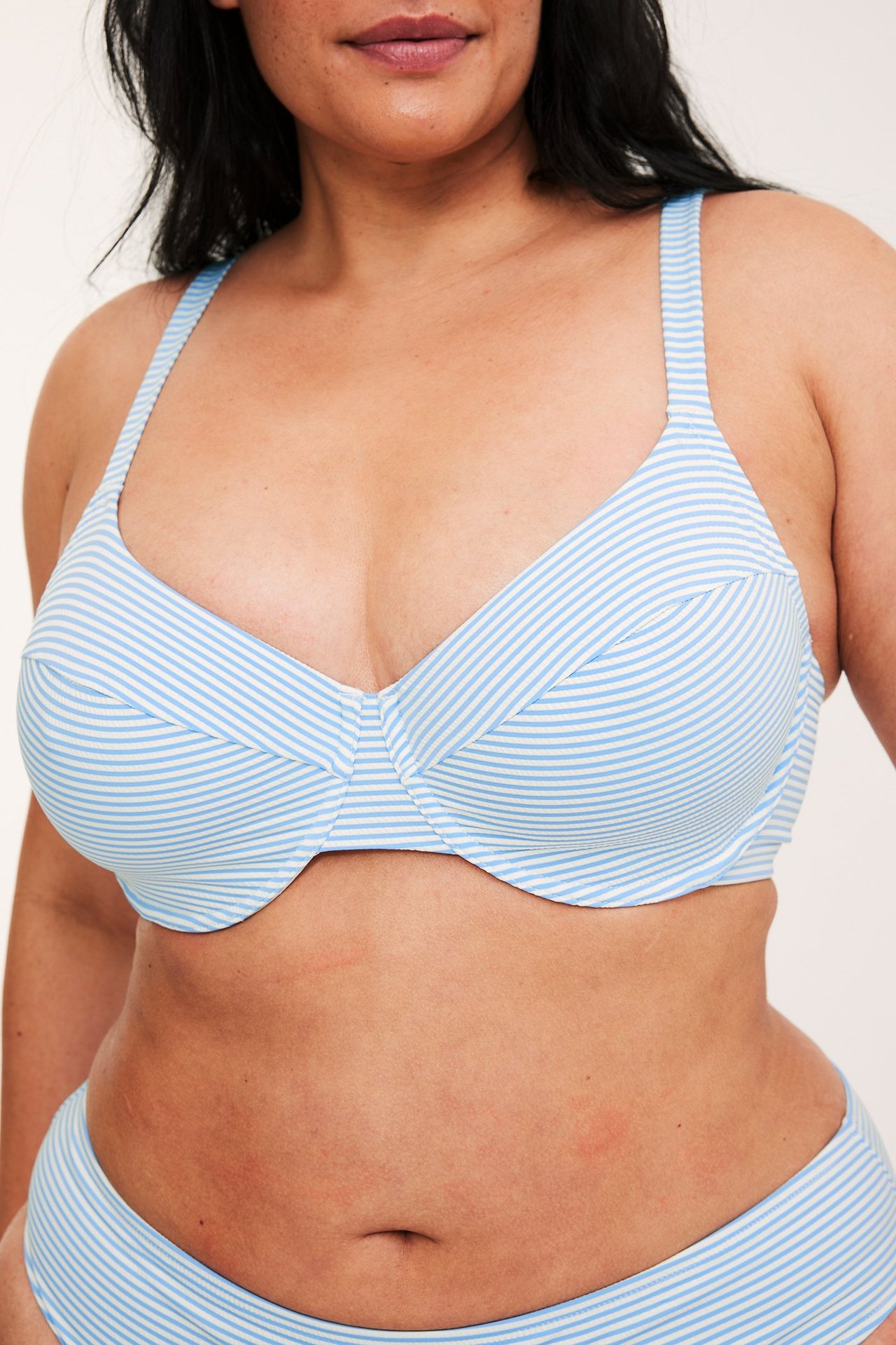 Lähikuva edestä naisesta, jolla on yllään raidallinen vaaleansinivalkoinen bikiniliivi ja yhteensopiva alaosa.