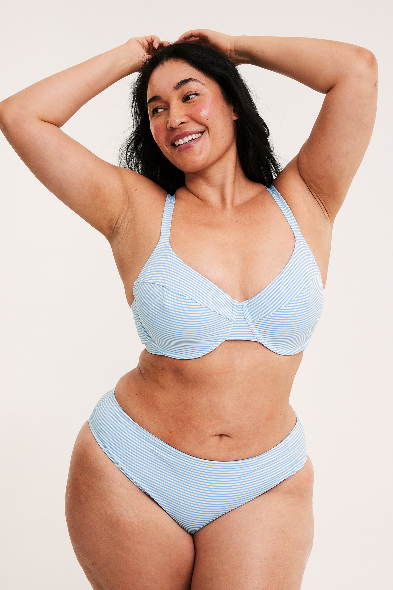 Framifrån, leende kvinna i ljusblå randig bikini-bh och matchande bikinitrosor.