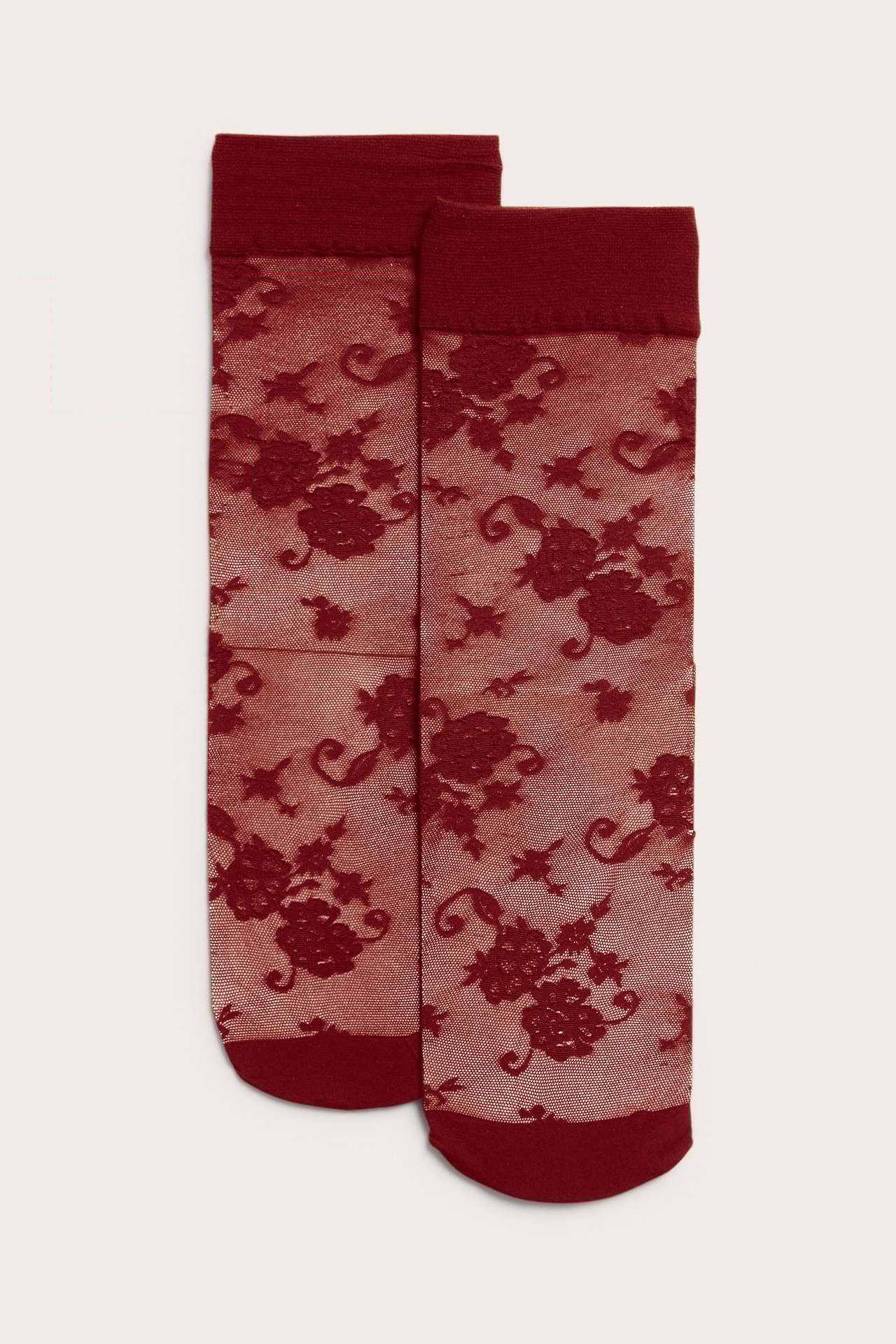 Widok z przodu pary czerwonych, przezroczystych skarpet nylonowych z kwiatowym wzorem koronkowym, jednolitymi ściągaczami i palcami.
