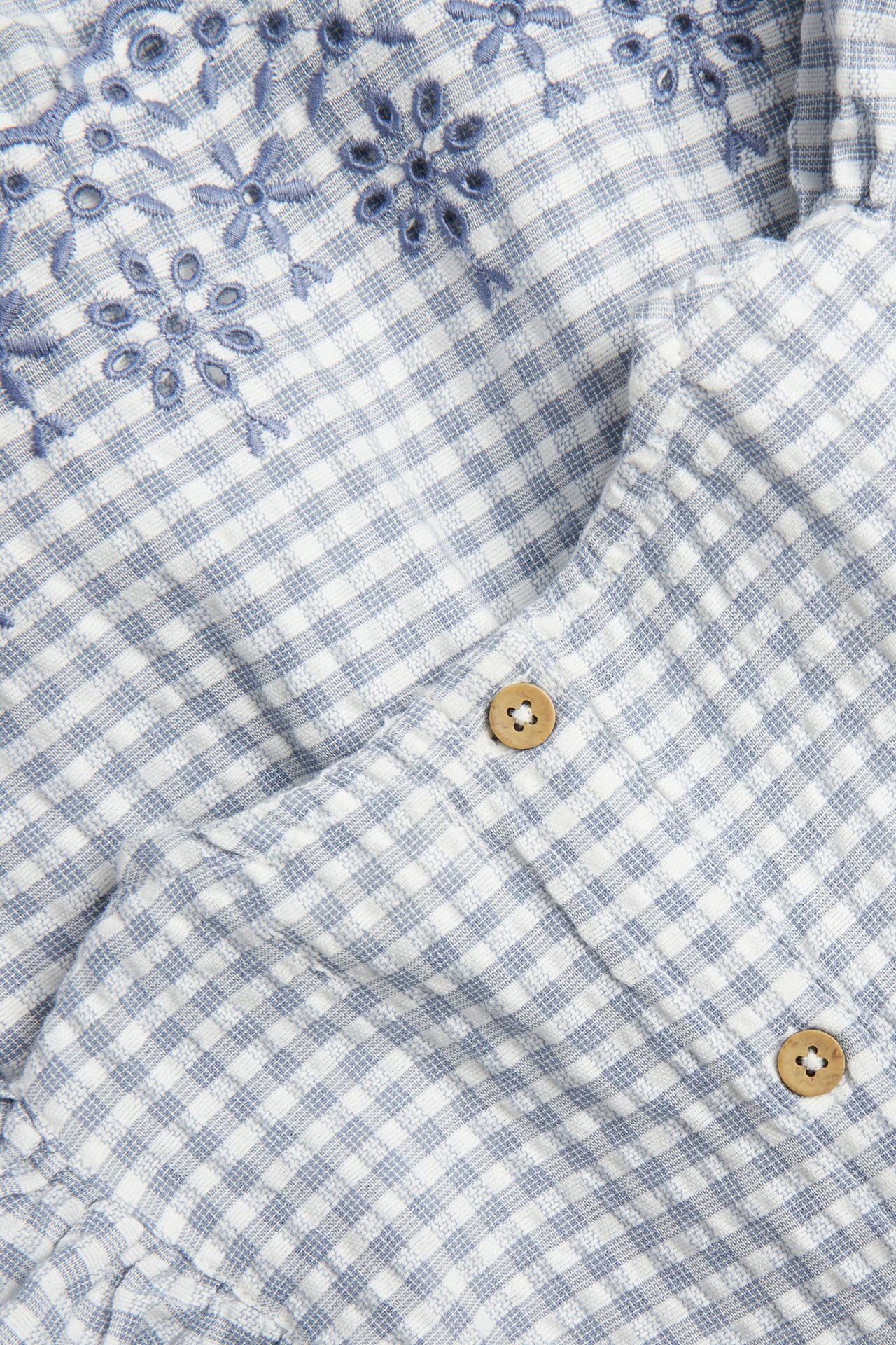 Zbliżenie na body niemowlęce w niebiesko-białą kratkę, z haftem w kwiaty i drewnianymi guzikami.