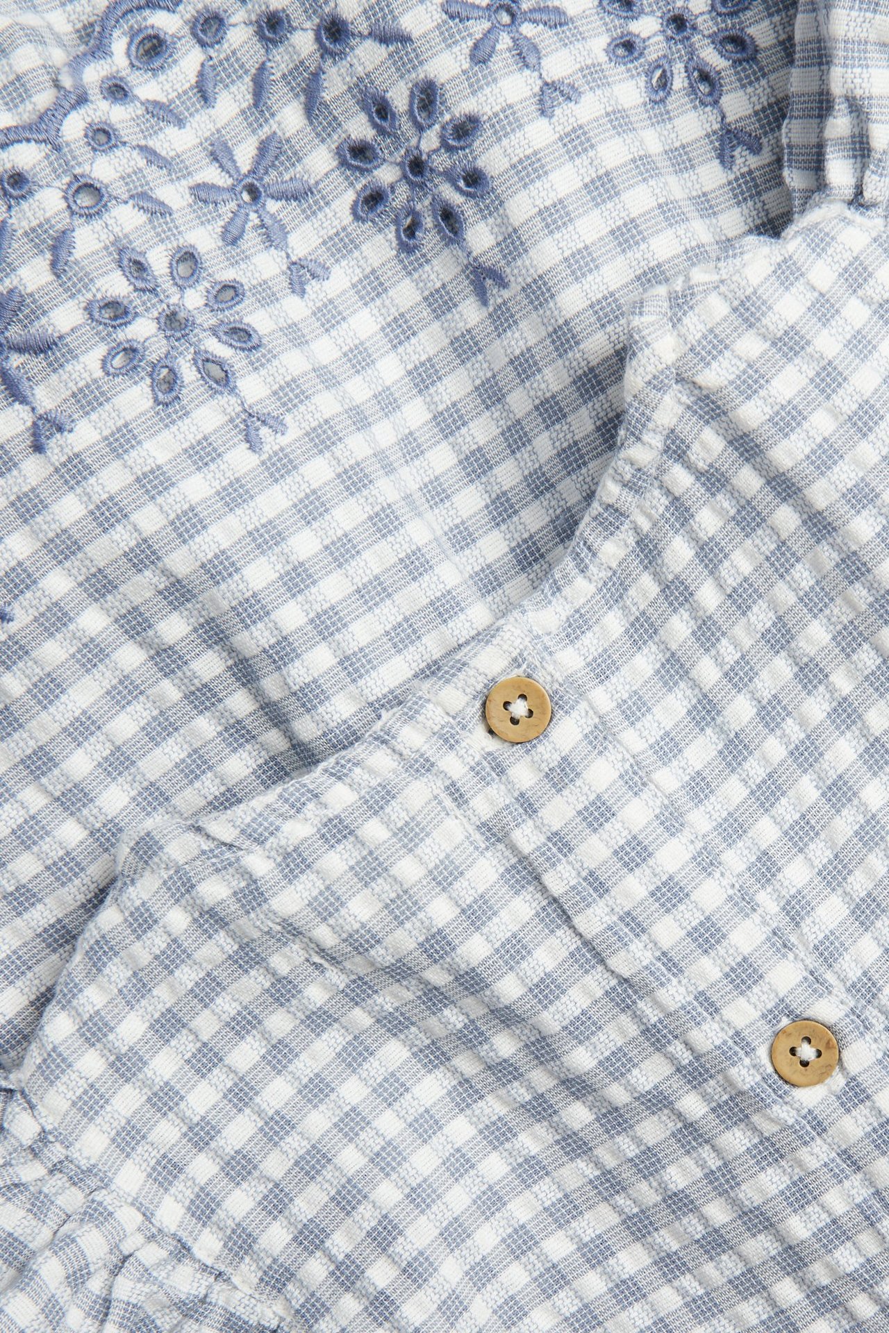 Zbliżenie na body niemowlęce w niebiesko-białą kratkę, z haftem w kwiaty i drewnianymi guzikami.