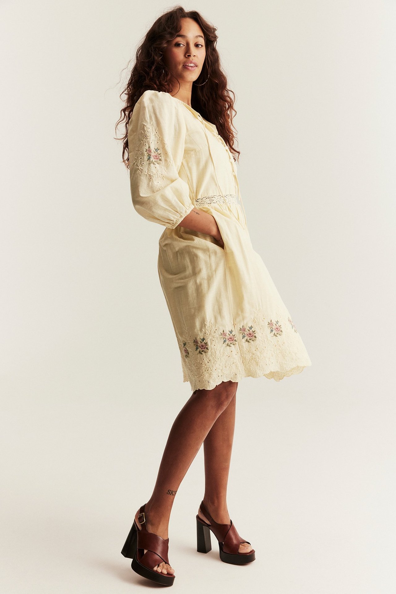 Framifrån: kvinna i ljusgul broderad kort klänning och mörkbruna platåsandaler.