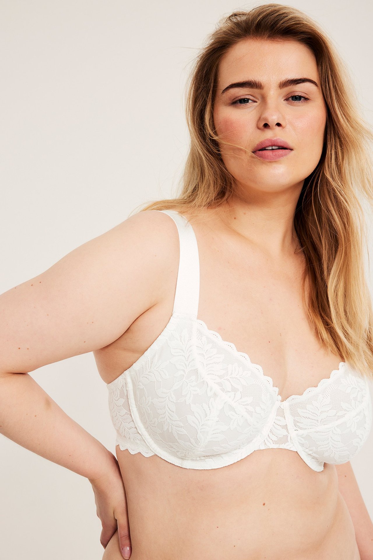 Frontvy av en kvinna som bär en offwhite bygelbh i spets med breda axelband och vågig kant.