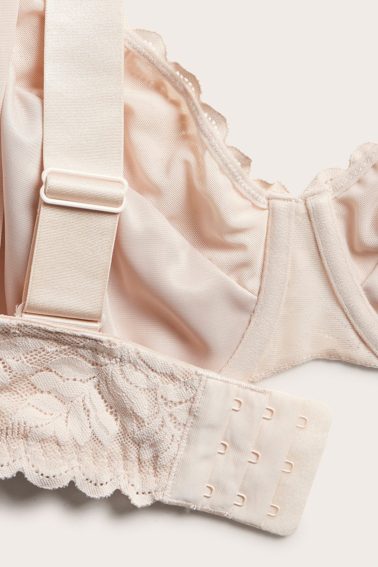 Lähikuva vaaleanpunaisista pitsisistä kaarituellisista rintaliiveistä, leveillä säädettävillä olkaimilla ja hakaskiinnityksellä.