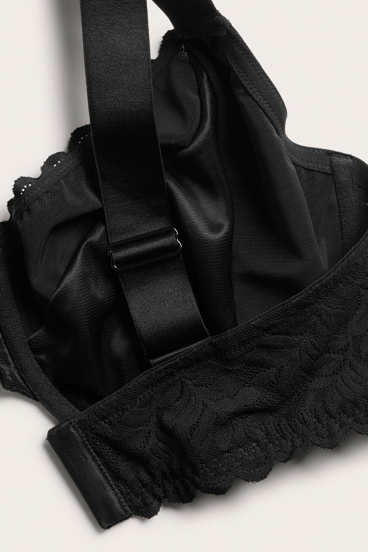 Lähikuva mustasta kaarituellisesta rintaliivistä, jossa on kukkakuvioinen pitsi ja leveät säädettävät olkaimet.