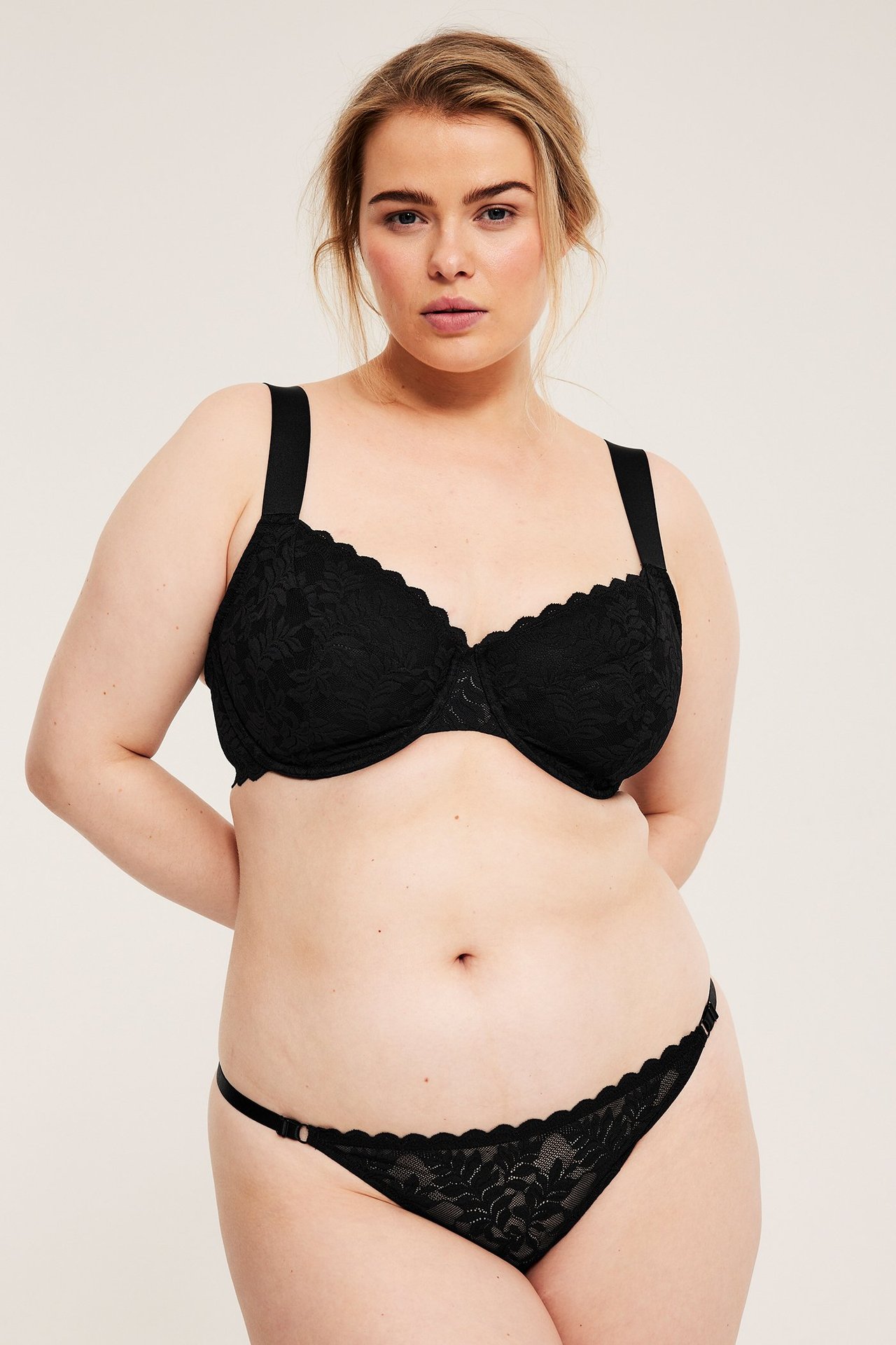 Widok z przodu: Kobieta w czarnym biustonoszu z fiszbinami i koronki z szerokimi ramiączkami oraz pasującymi koronkowymi figami.
