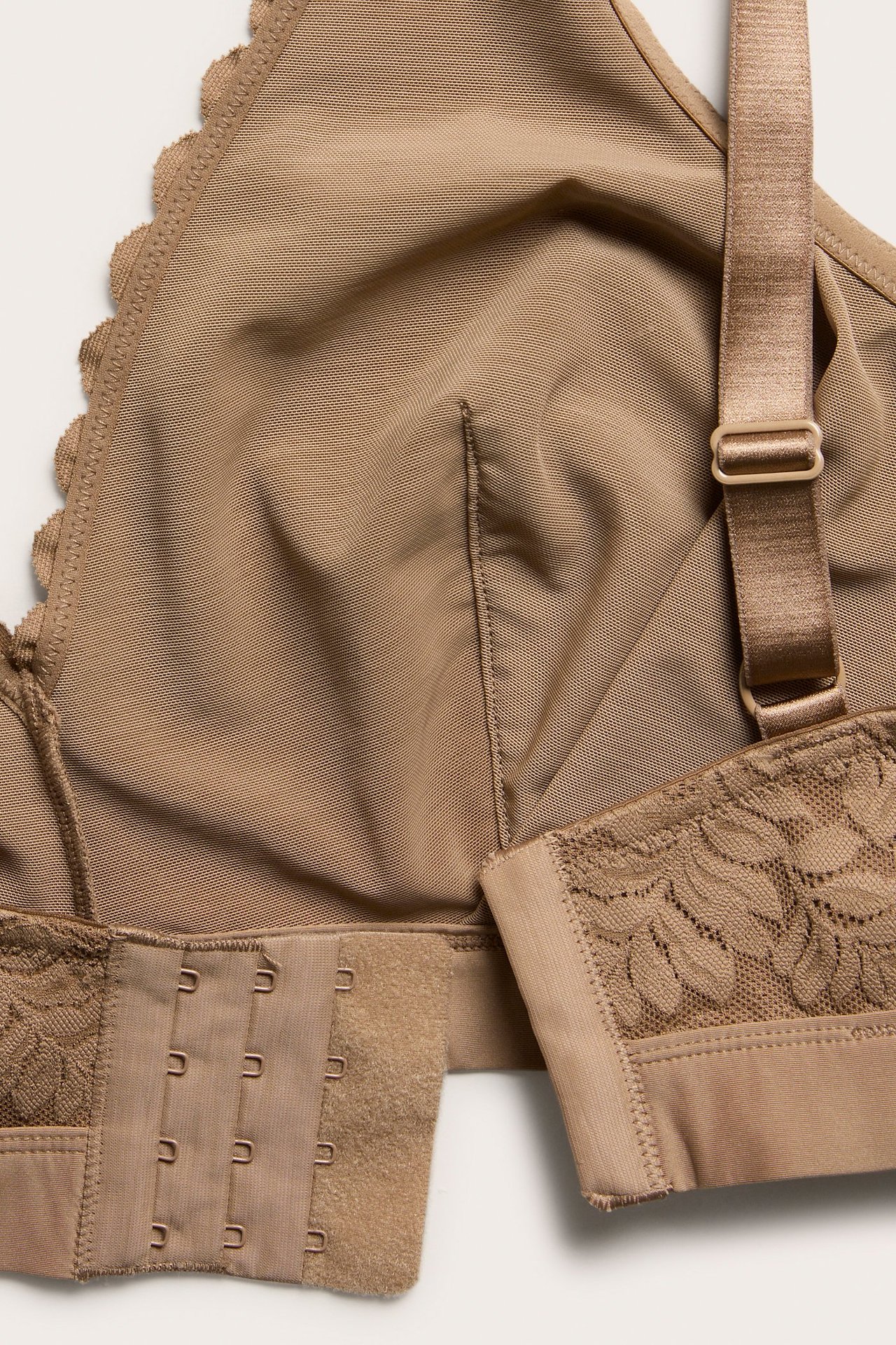 Nærbilde av en beige blonde-bralette med justerbare stropper, hekte-lukking og bølget kant.