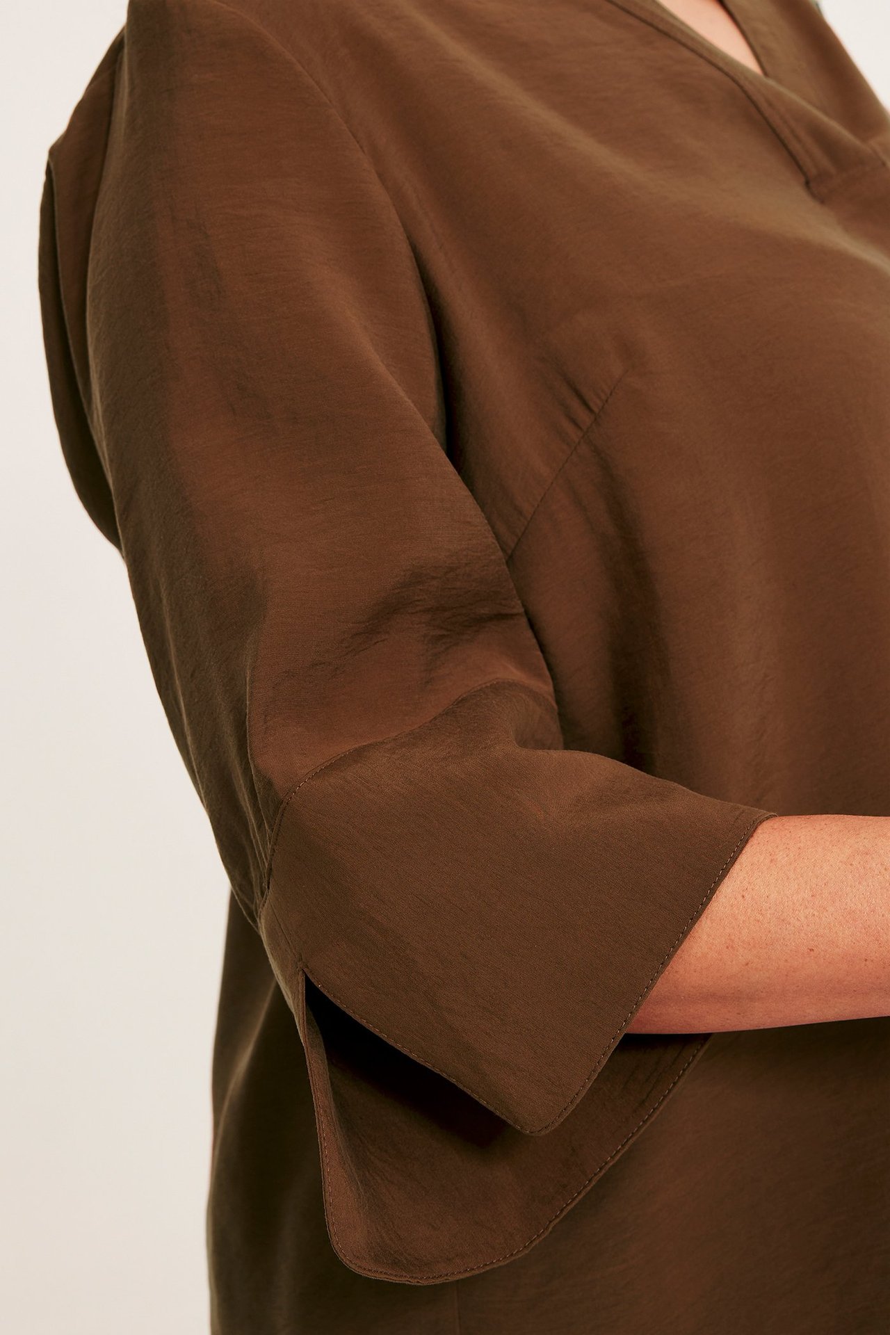 Zbliżenie kobiety w brązowej bluzce z dekoltem w serek, szerokimi rękawami 3/4 i jedwabistym połyskiem.