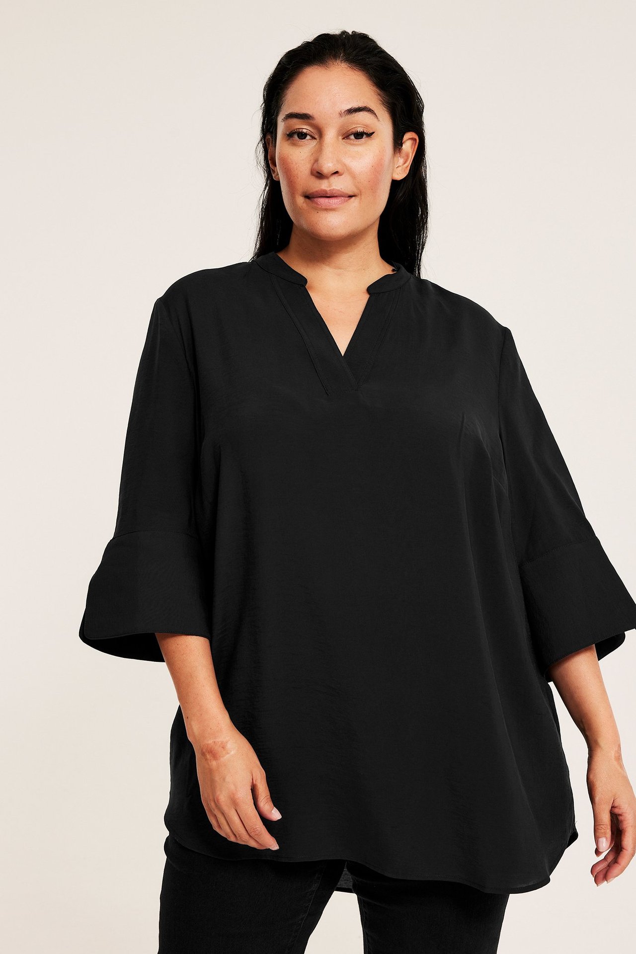 Widok z przodu: kobieta w czarnej bluzce z dekoltem V, luźnej, z rękawami 3/4 i rozszerzanymi mankietami.