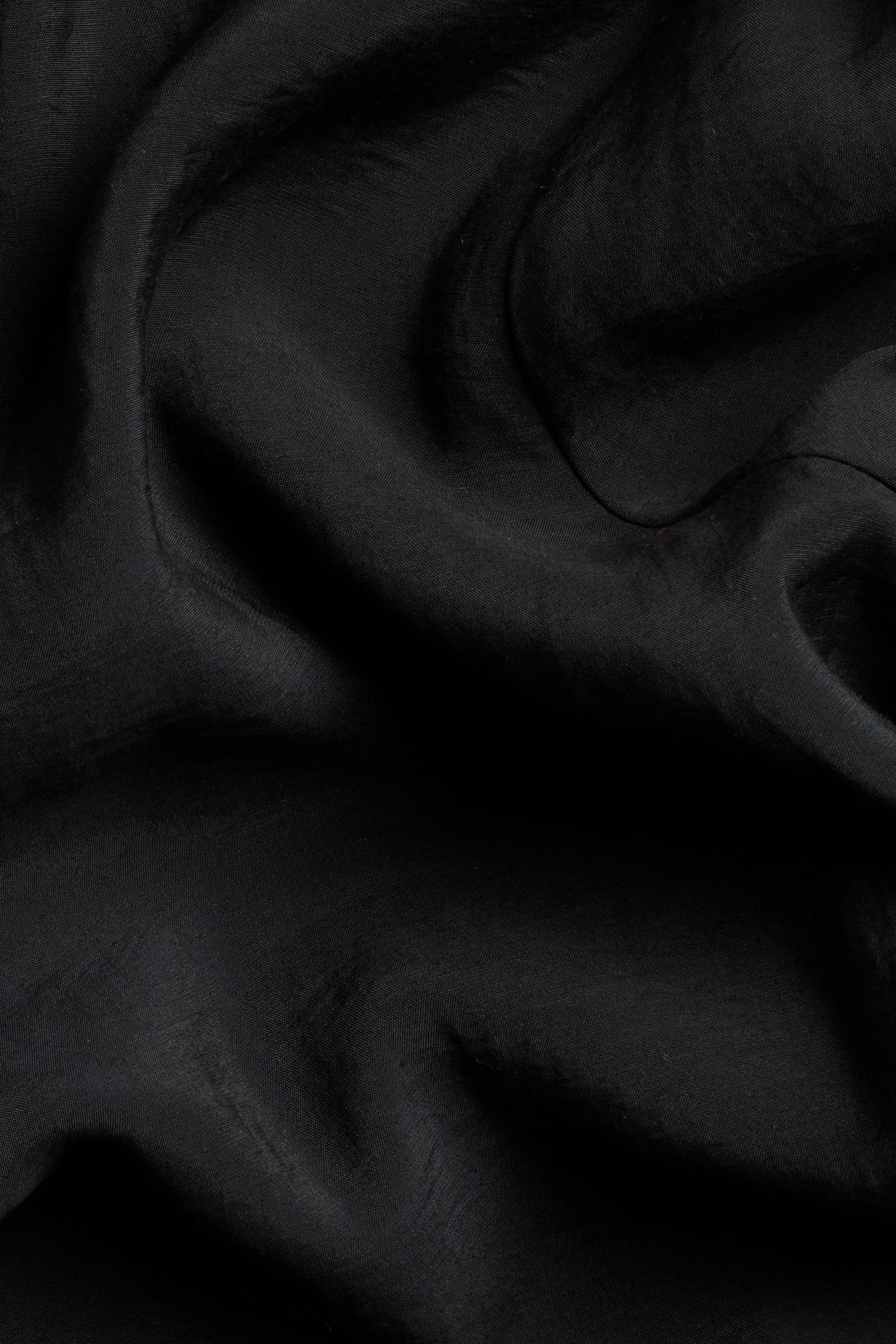 Zbliżenie czarnego materiału modalowo-poliestrowego o jedwabistym połysku i miękkich fałdach.