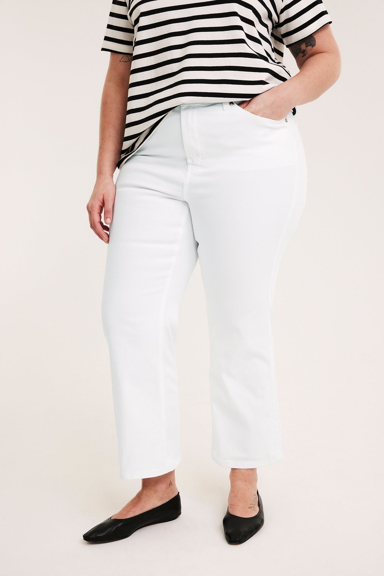 Naisen etukuva valkoisissa korkeavyötäröisissä cropped flare -farkuissa, raidallisessa t-paidassa ja mustissa ballerinakengissä.