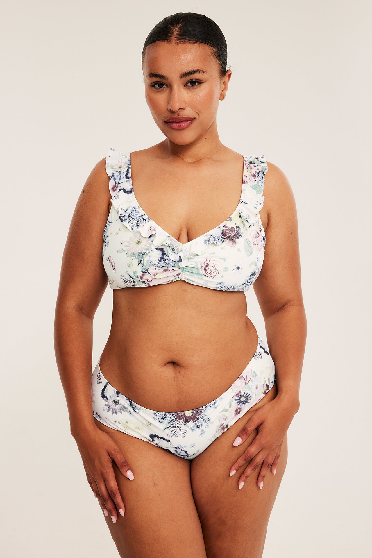 Frontbilde, kvinnelig modell i en hvit blomstret bikini med volanger.