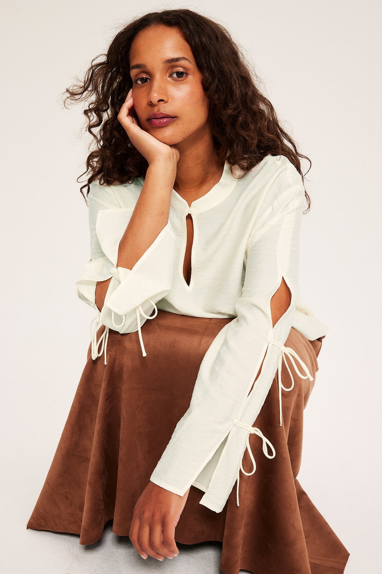 Framifrån, kvinna bär offwhite blus med knytdetaljerade långa ärmar och en brun A-linjeformad kjol.