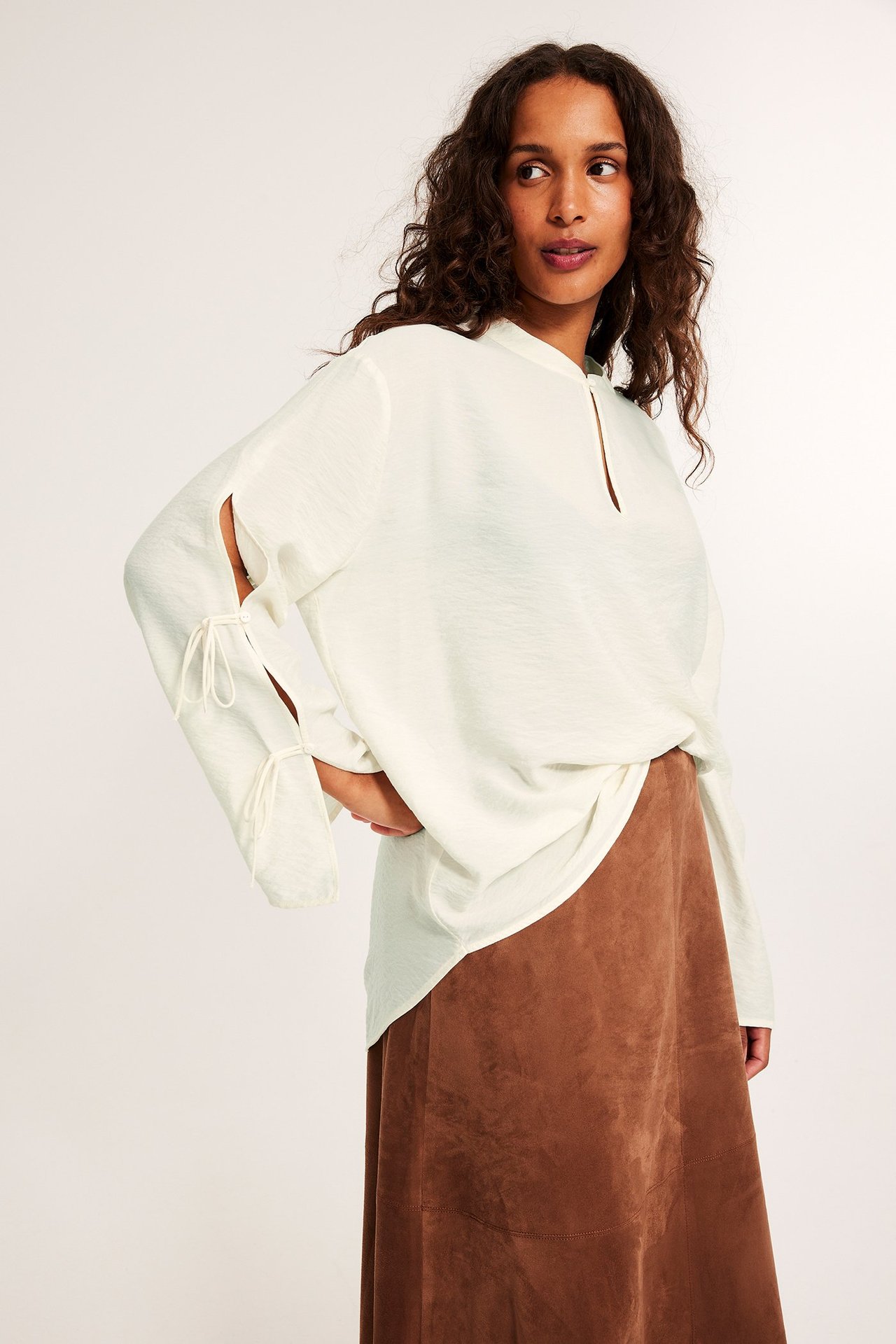 Frontvy av en kvinna i en lös offwhite-blus med knytdetaljer på ärmarna, stylad med en brun kjol.