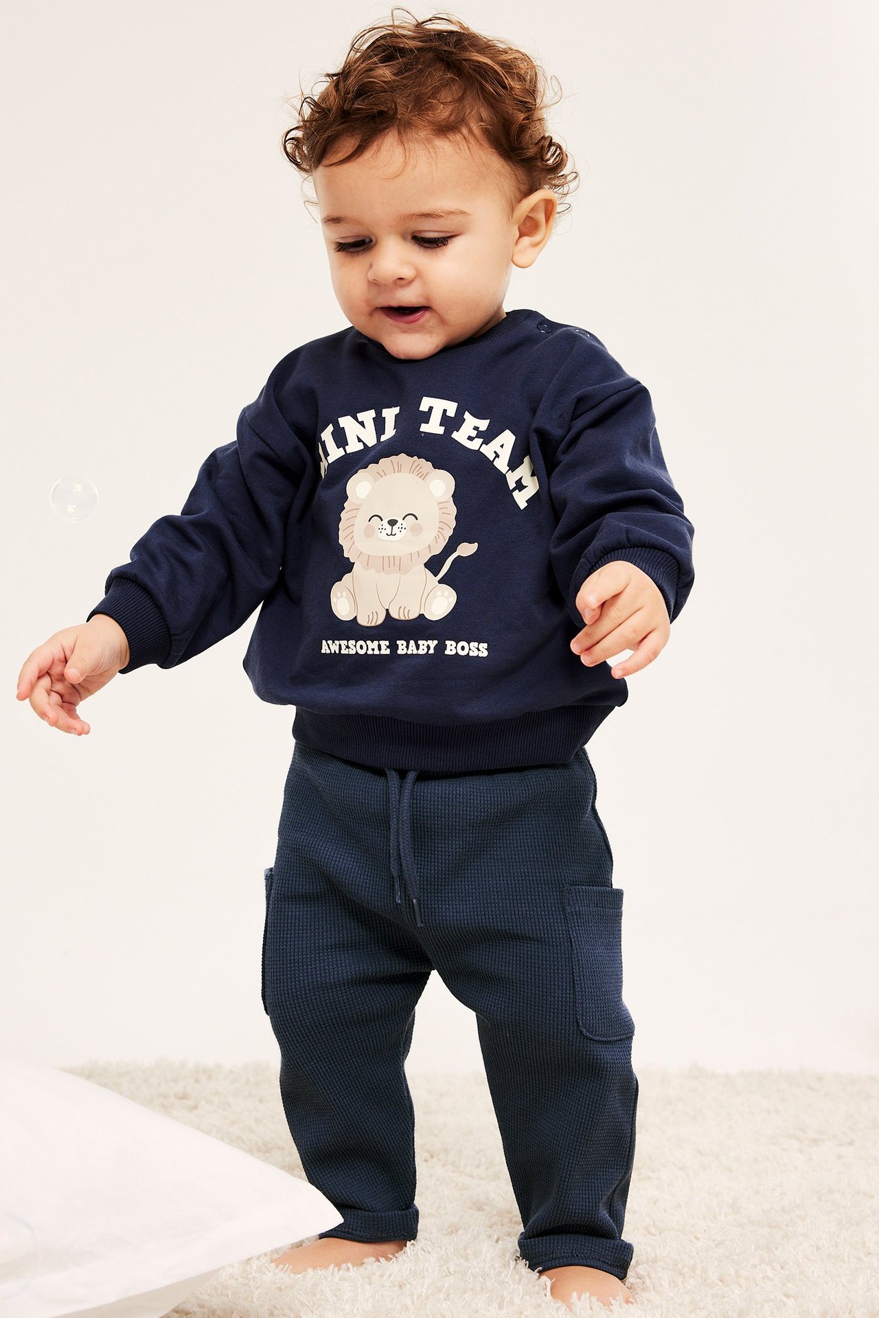 Baby, frontbilde: blå vaffelvevde bukser med sidelommer og snøring, samt marineblå løvegenser.