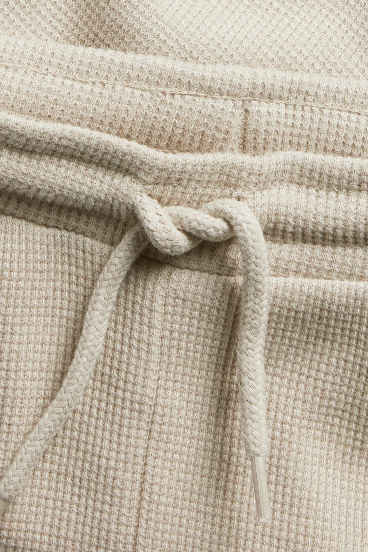 Nærbilde av beige vaffelbukser med en knyttet snøring i midjen.