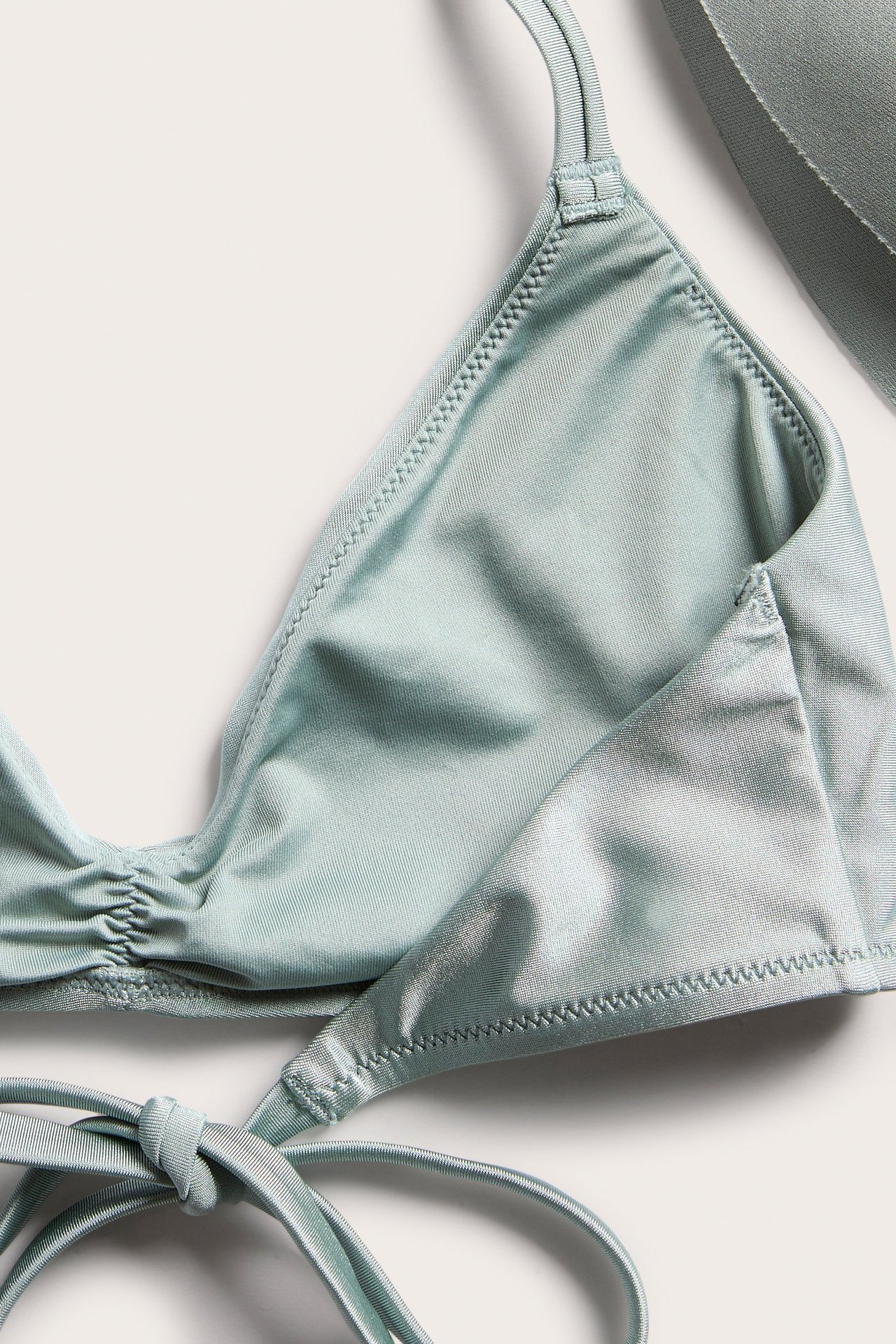 Nærbilde av en lysegrønn vattert trekant-bikinitopp med knyting og rynkede detaljer.