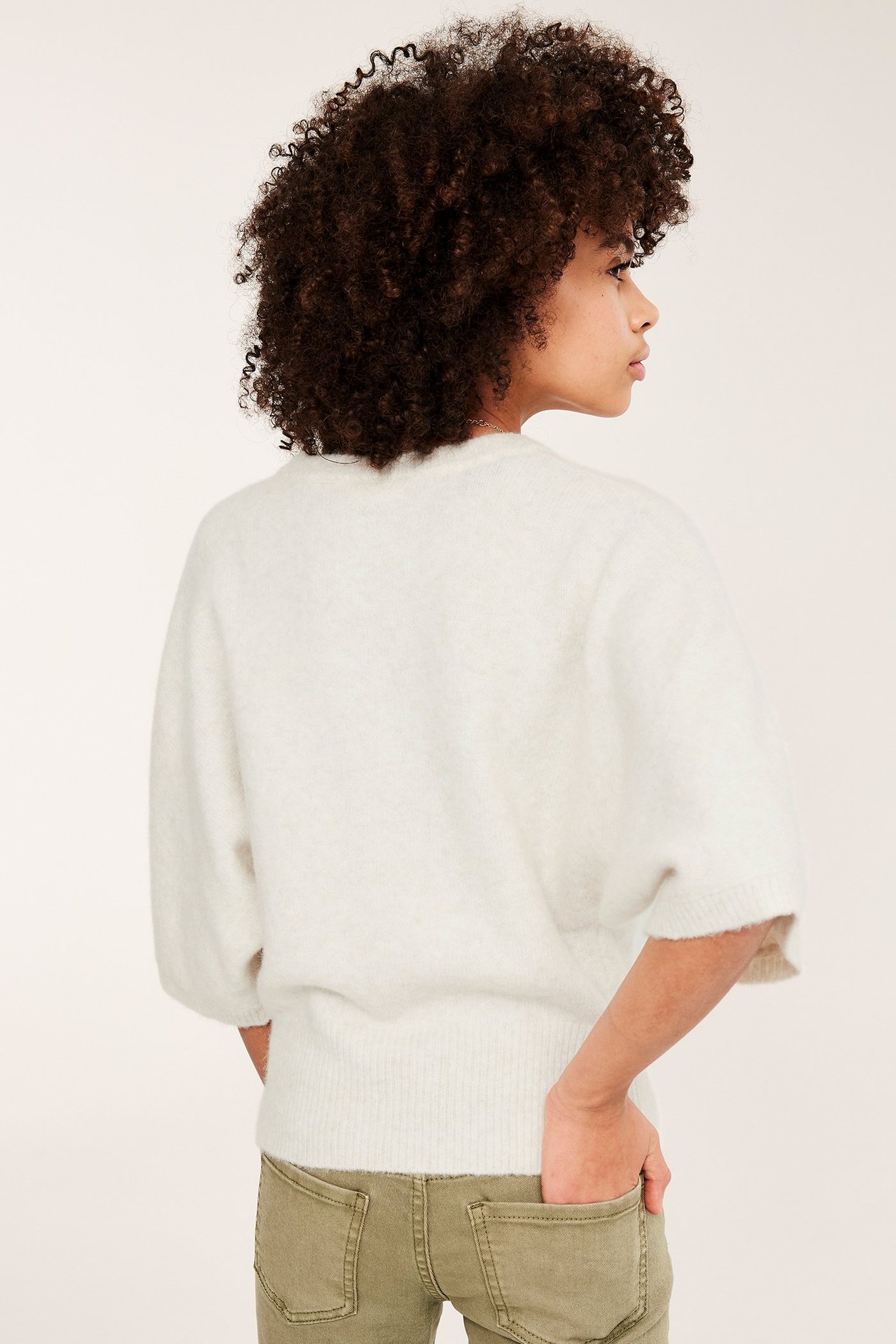 Widok z boku dziecka w białym melanżowym topie dzianinowym z krótkimi rękawami i zielonych spodniach.