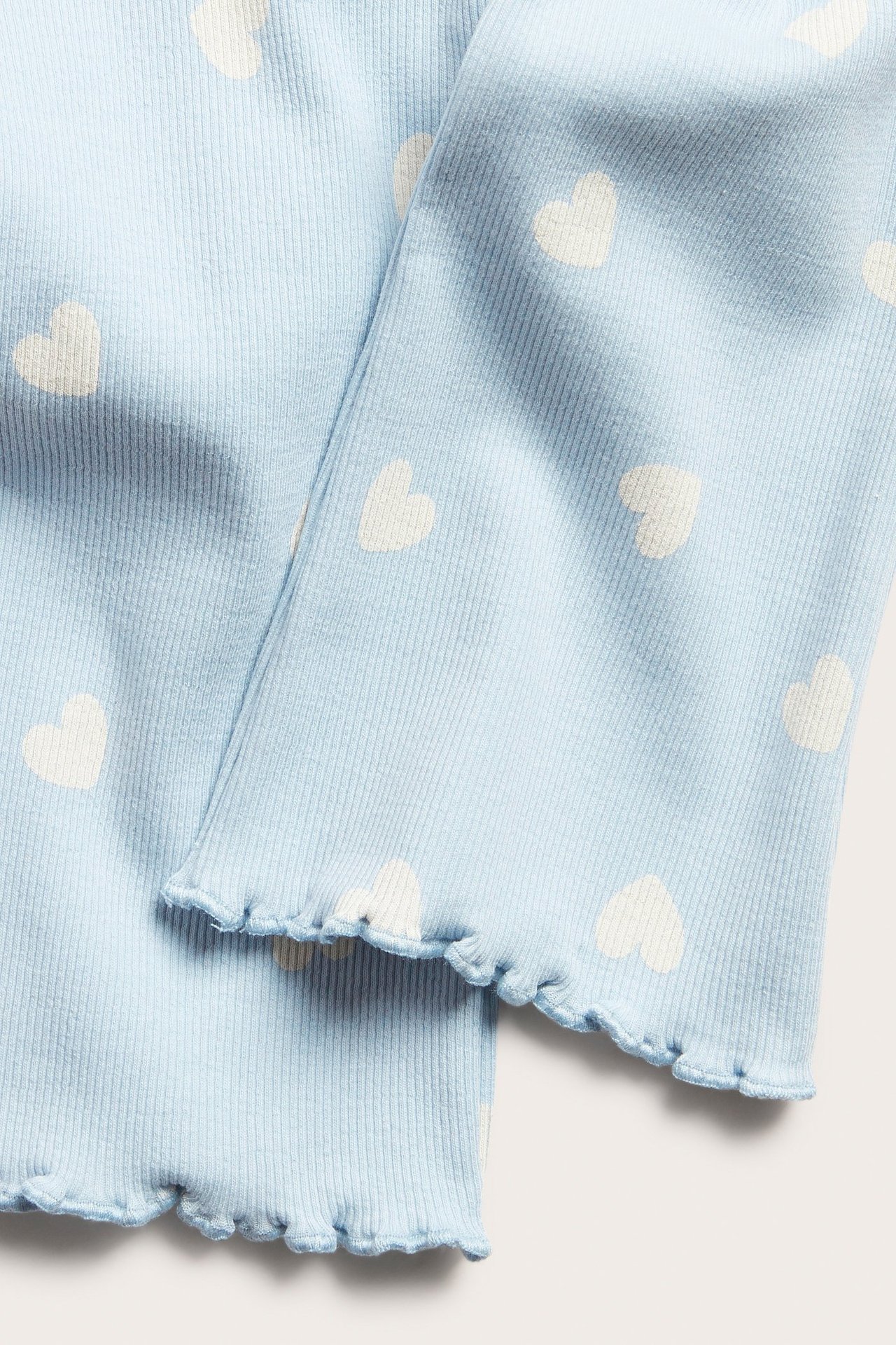 Nærbilde av lyseblå ribbestrikkede leggings med hvitt hjertemønster og bølgete baby lock-kant.