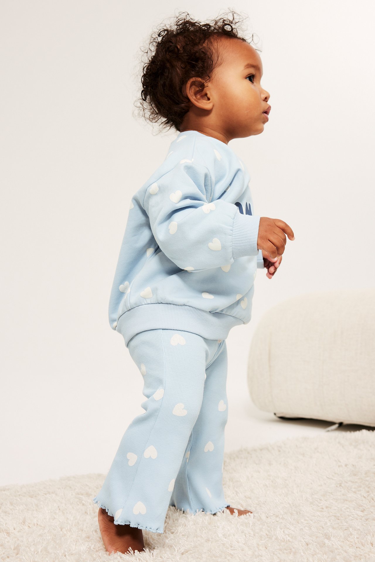 Sidebilde av baby i lyseblå ribbestrikket flare-leggings med hvite hjerter og matchende genser.