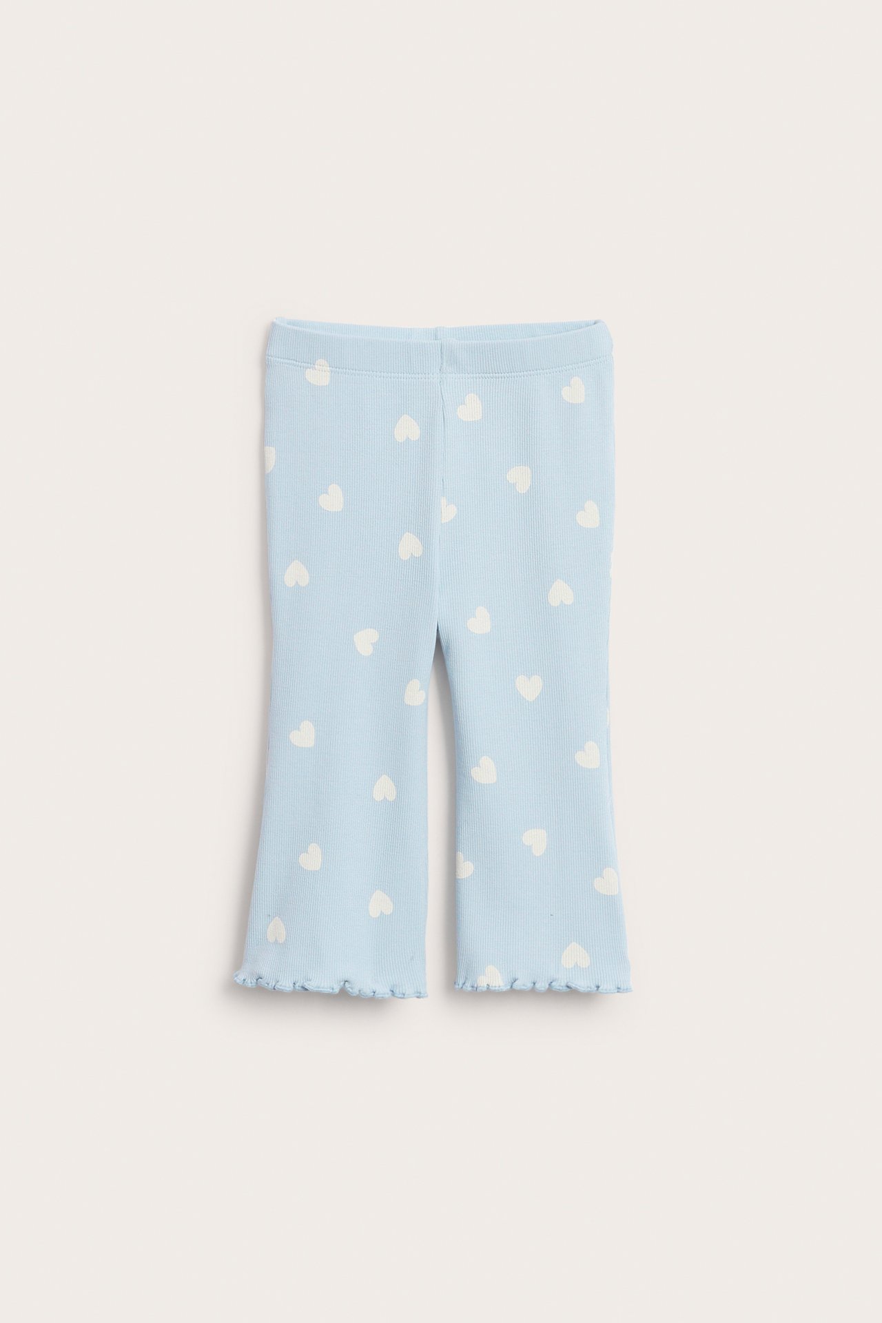 Frontvy, babyens lyseblå ribbestrikkede flare-leggings med hvitt hjertemønster og bølgete kant.