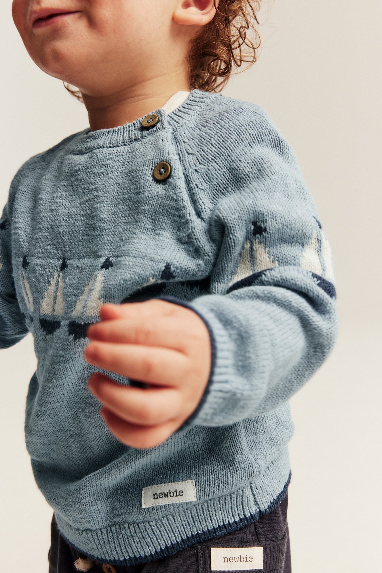 Lähikuva edestä vauvasta, jolla on vaaleansininen neulottu puuvillapusero purjevenejakardilla ja olkapäänapeilla.