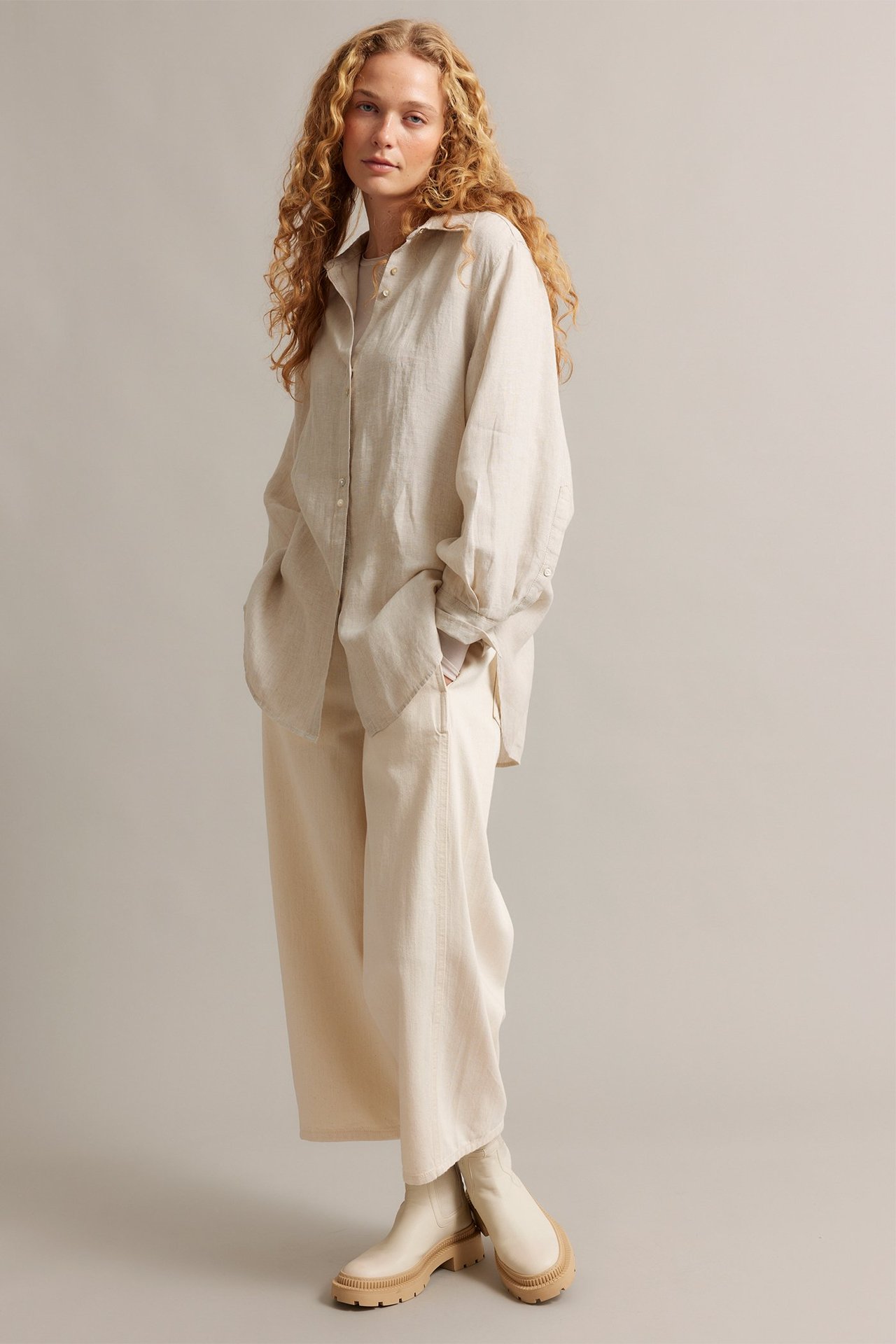 Framifrån: kvinna i beige oversize linneskjorta, ljusbeige vida byxor och gräddfärgade kängor.