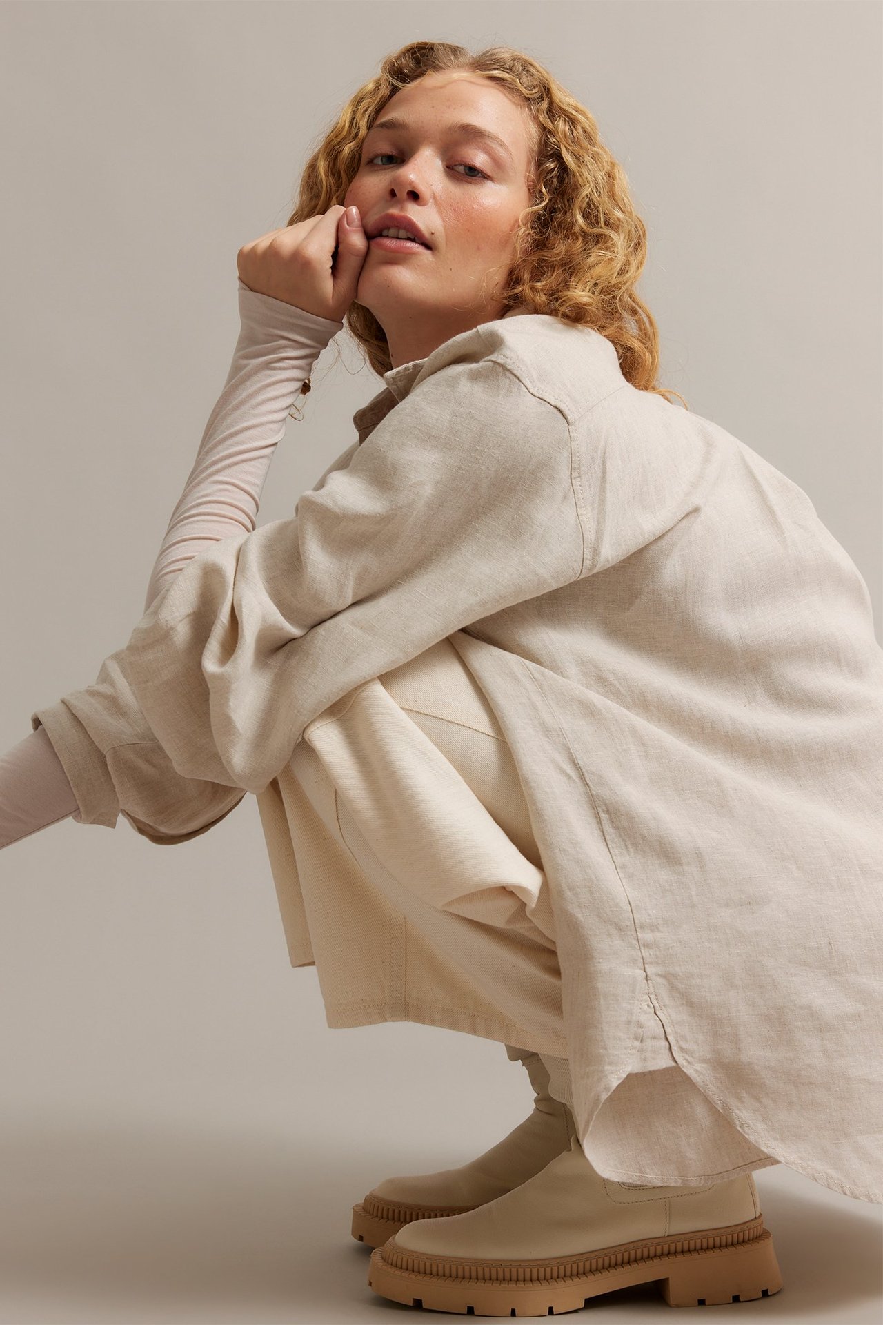 Kvinna i beige melerad linneskjorta över ljus topp, med beiga byxor och grova kängor.