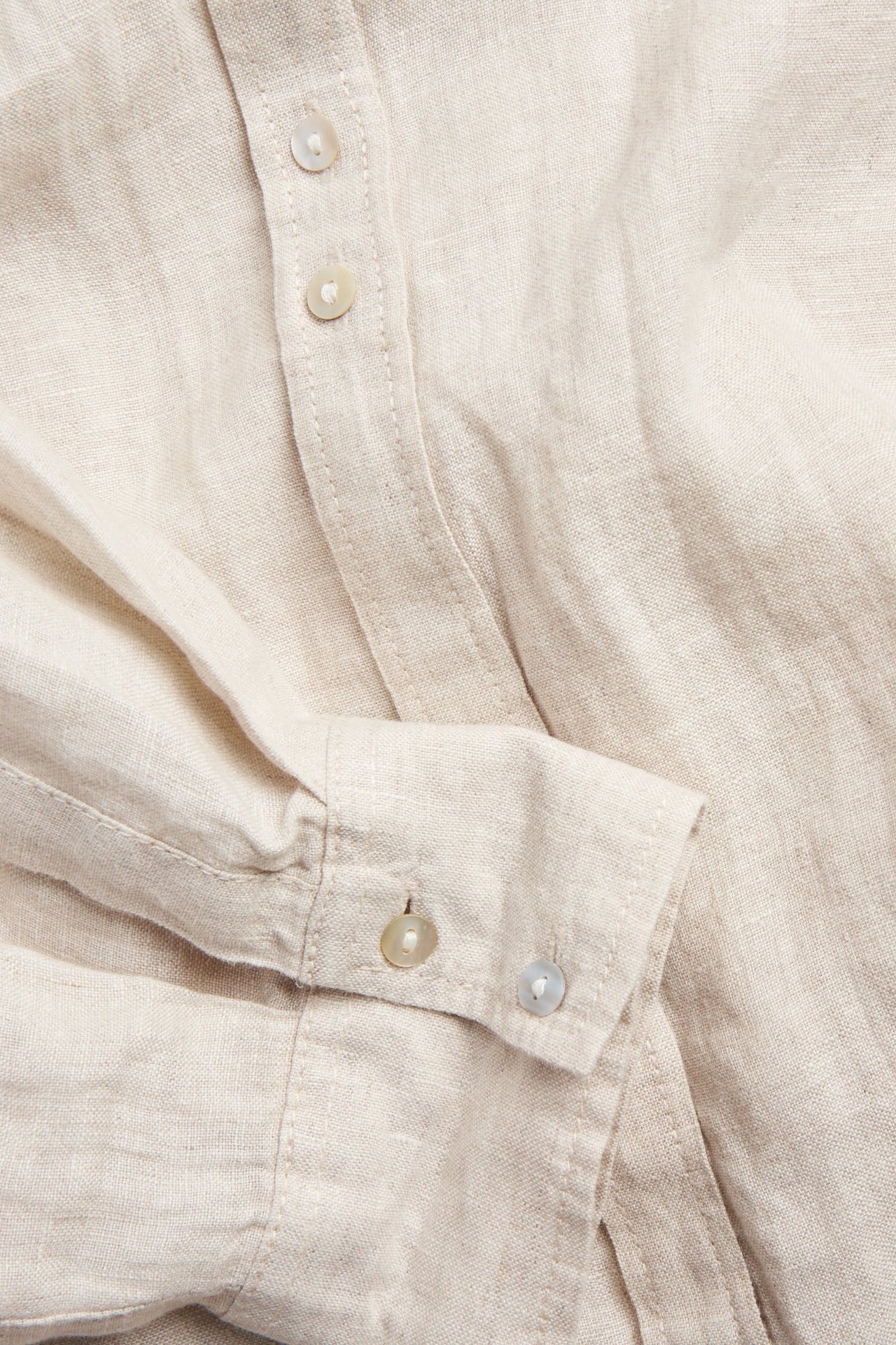 Zbliżenie beżowej melanżowej koszuli lnianej z guzikami z masy perłowej na plisie i mankiecie.
