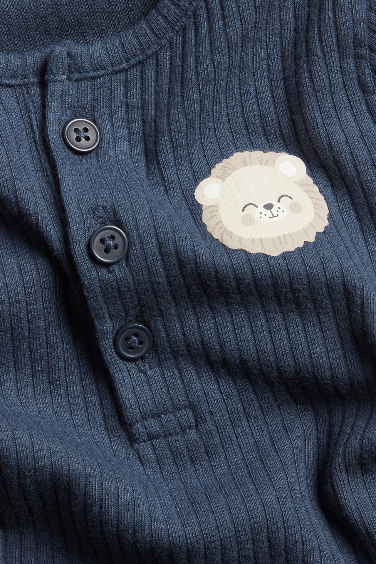 Nærbilde forfra av en mørkeblå ribbet langermet babybody med løvetrykk og knapper foran.