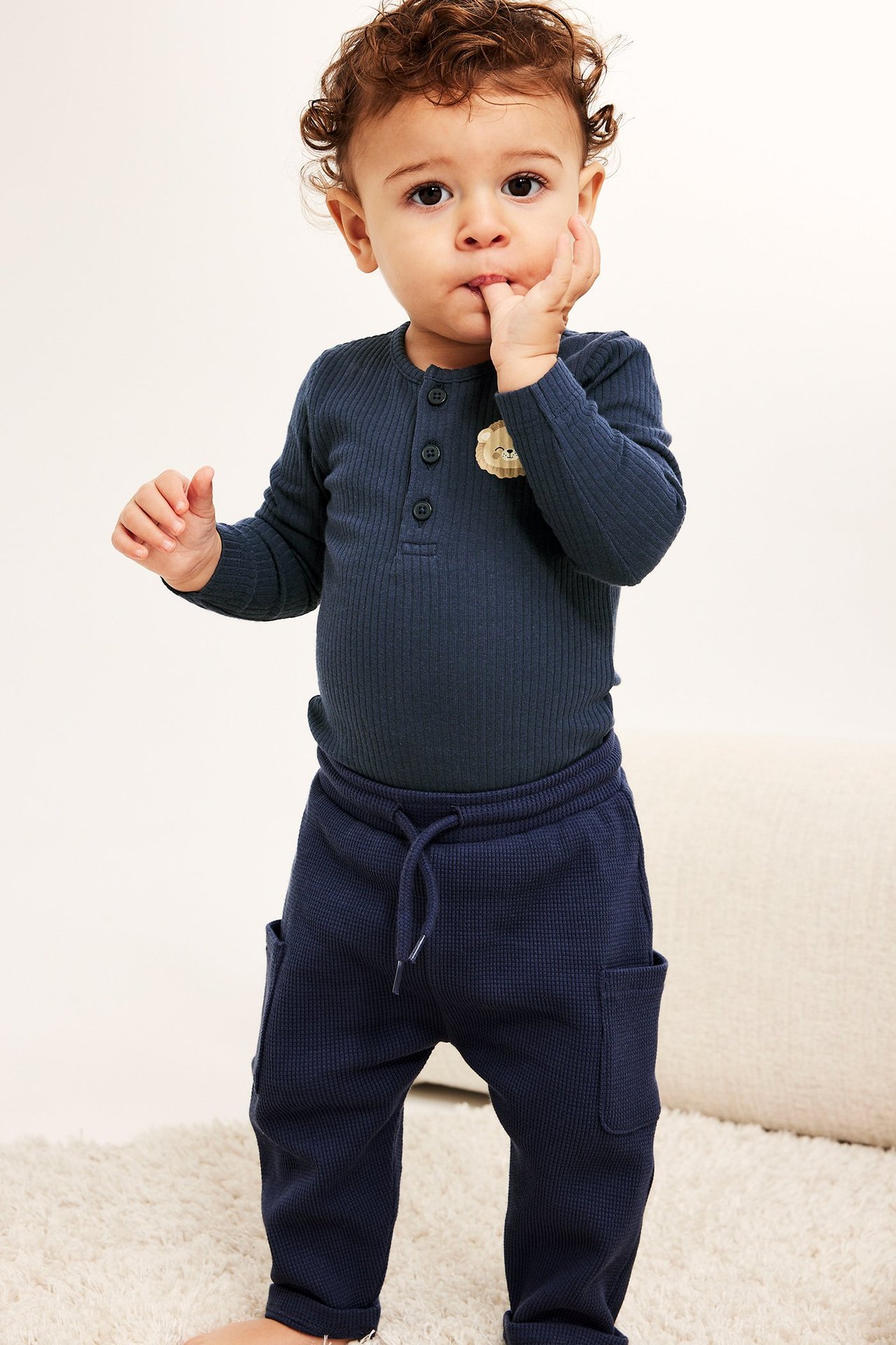 Från framsidan: baby i mörkblå ribbad långärmad body med lejonprint och mörkblå våfflade sweatpants.