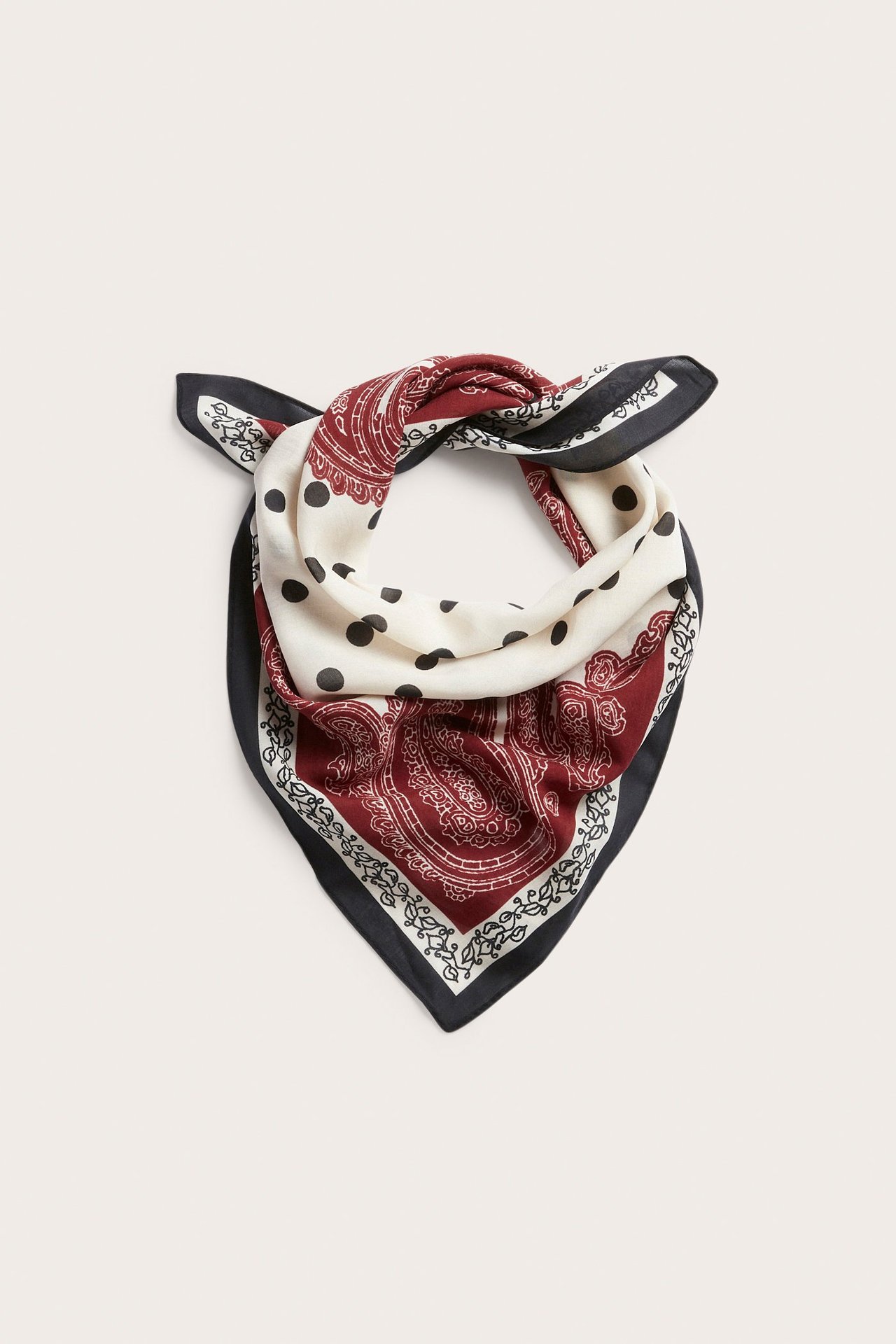 Edestä, taiteltu kuviollinen huivi vaaleanbeigenä mustilla pilkuilla, tummanpunaisella paisleyllä ja mustalla kuviollisella reunalla.