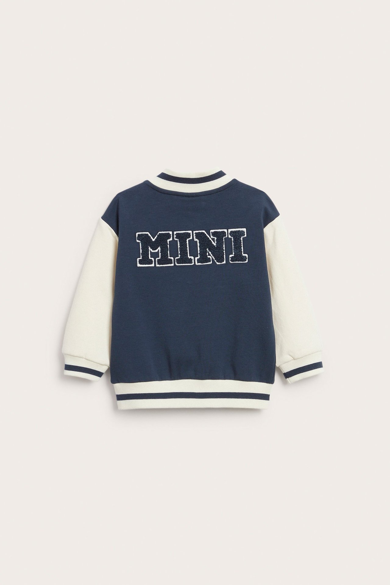 Bakifrån: babyjacka i mörkblått och krämvitt med 'MINI' frottéapplikation och ribbstickade kanter.