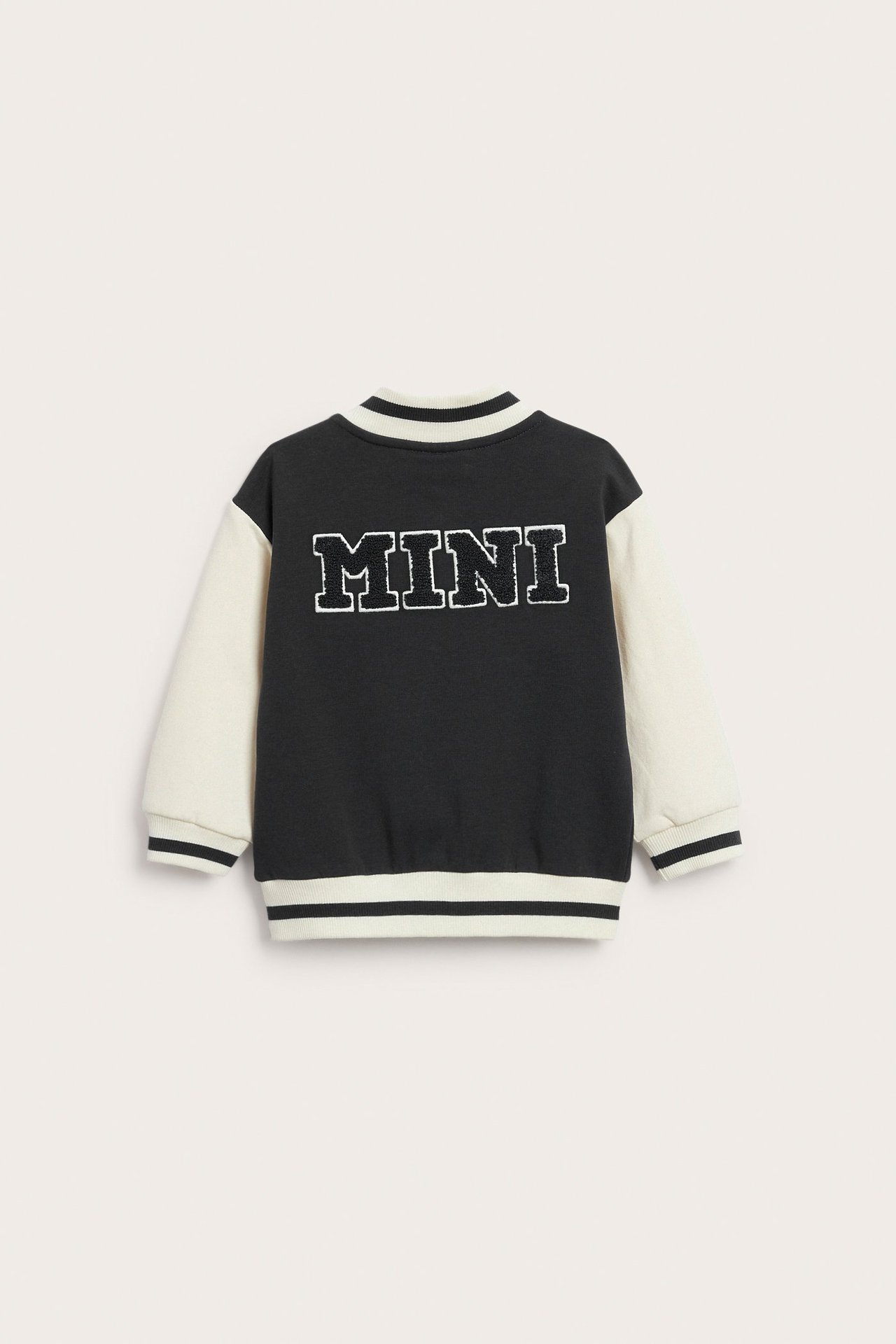 Bakfra av en svart og offwhite baseballjakke for barn med 'MINI' frottéapplikasjon og stripete ribb.