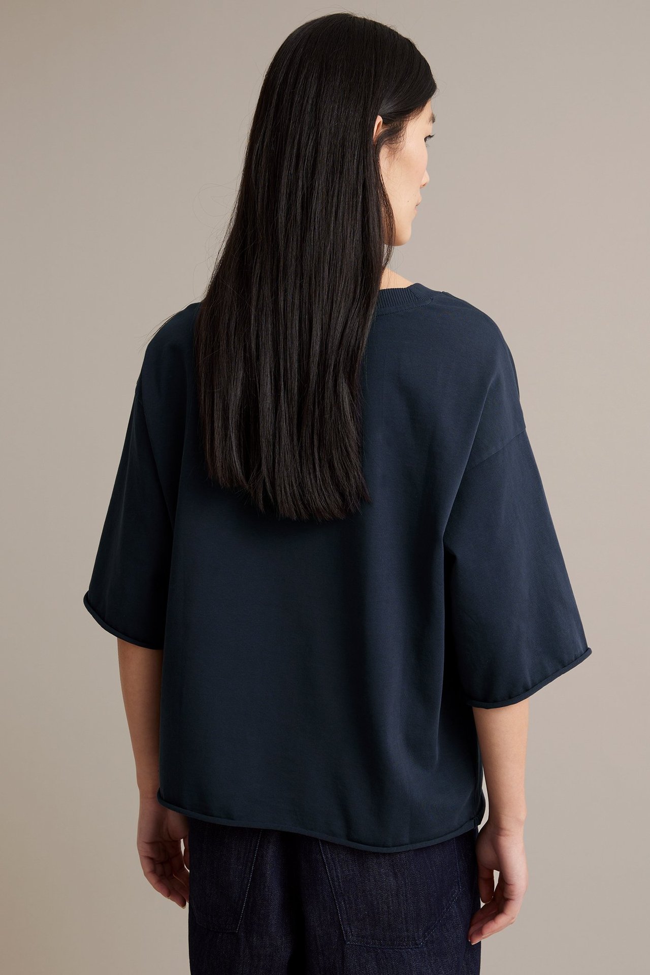 Människa i blå T-shirt i grov trikå, tvättad look, råa fållar, bakvy.
