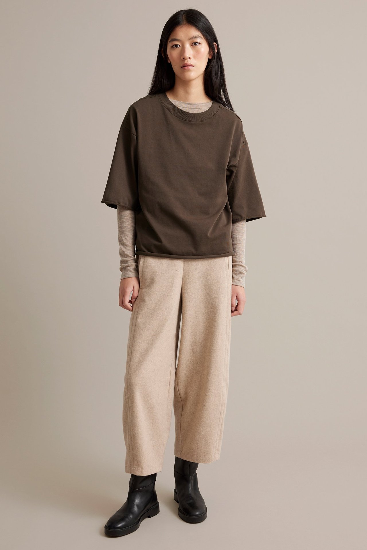 Nainen puvussa ruskea puuvillainen T-paita, beige housut ja mustat bootsit.