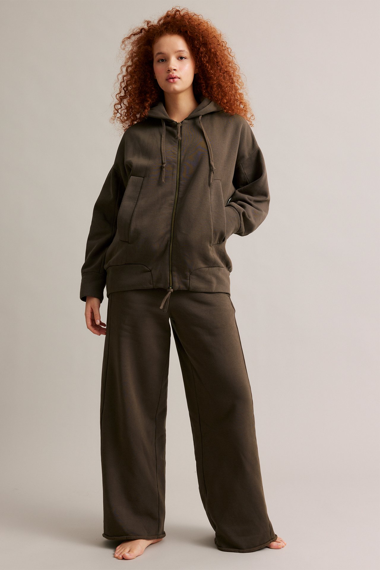 Edestä nainen ruskeassa puuvillasekoite vetoketjuhupparissa ja yhteensopivissa leveissä collegehousuissa.